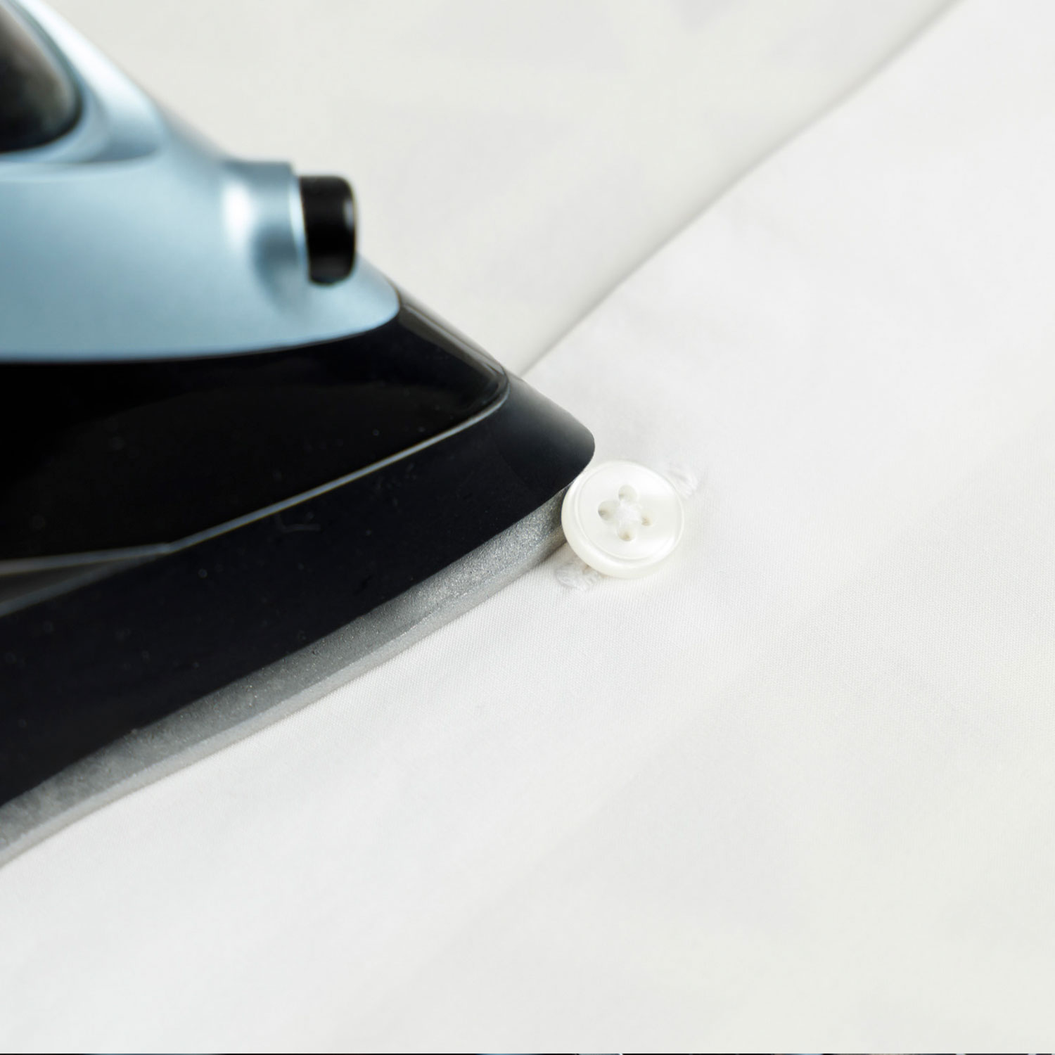 Una plancha está planchando un botón de camisa blanca.