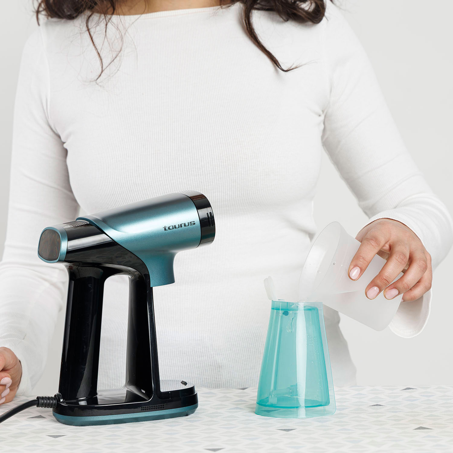 Una persona vierte agua en un recipiente azul junto a una plancha de vapor.
