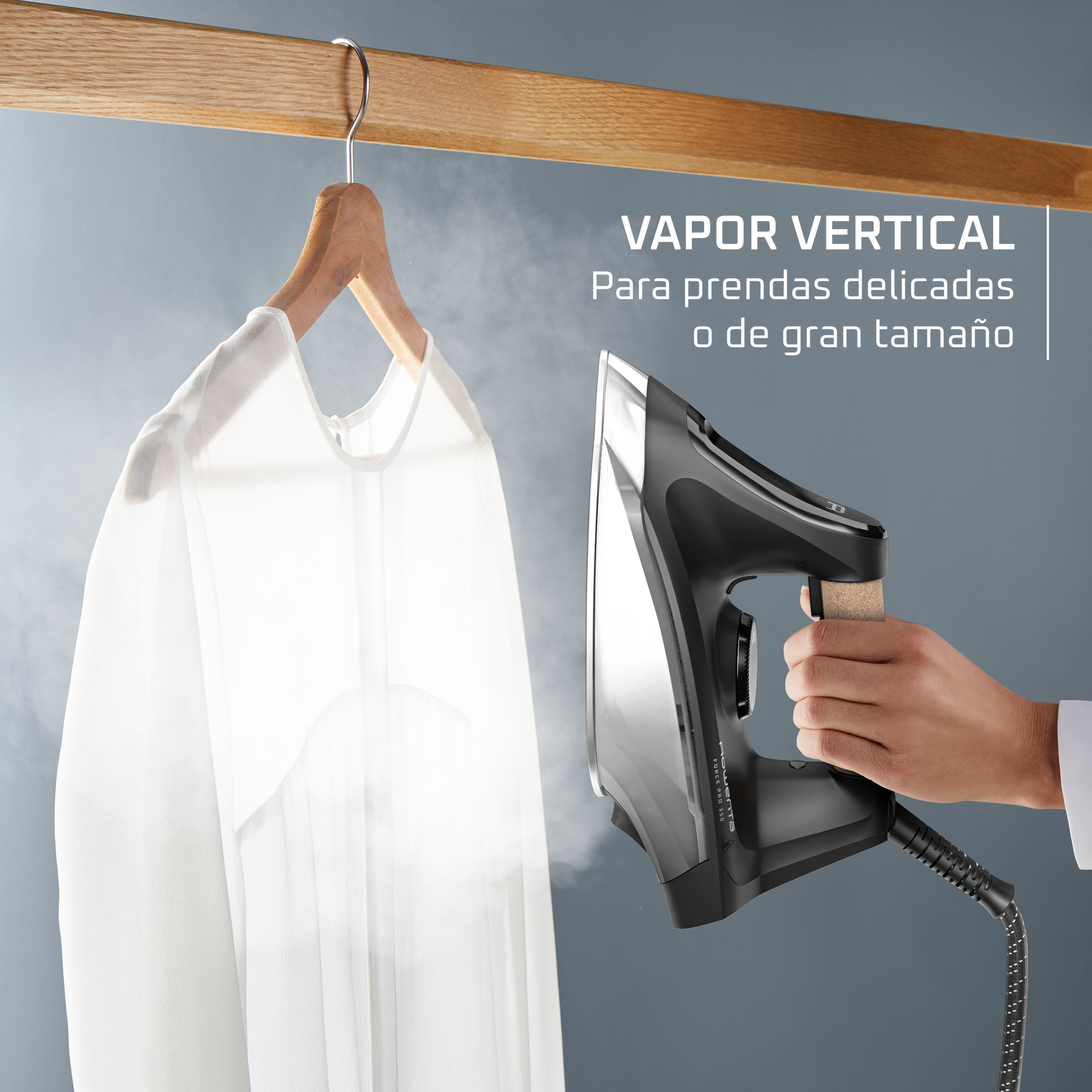 Una mano sostiene una plancha de vapor, vaporizando una camisa blanca colgada.