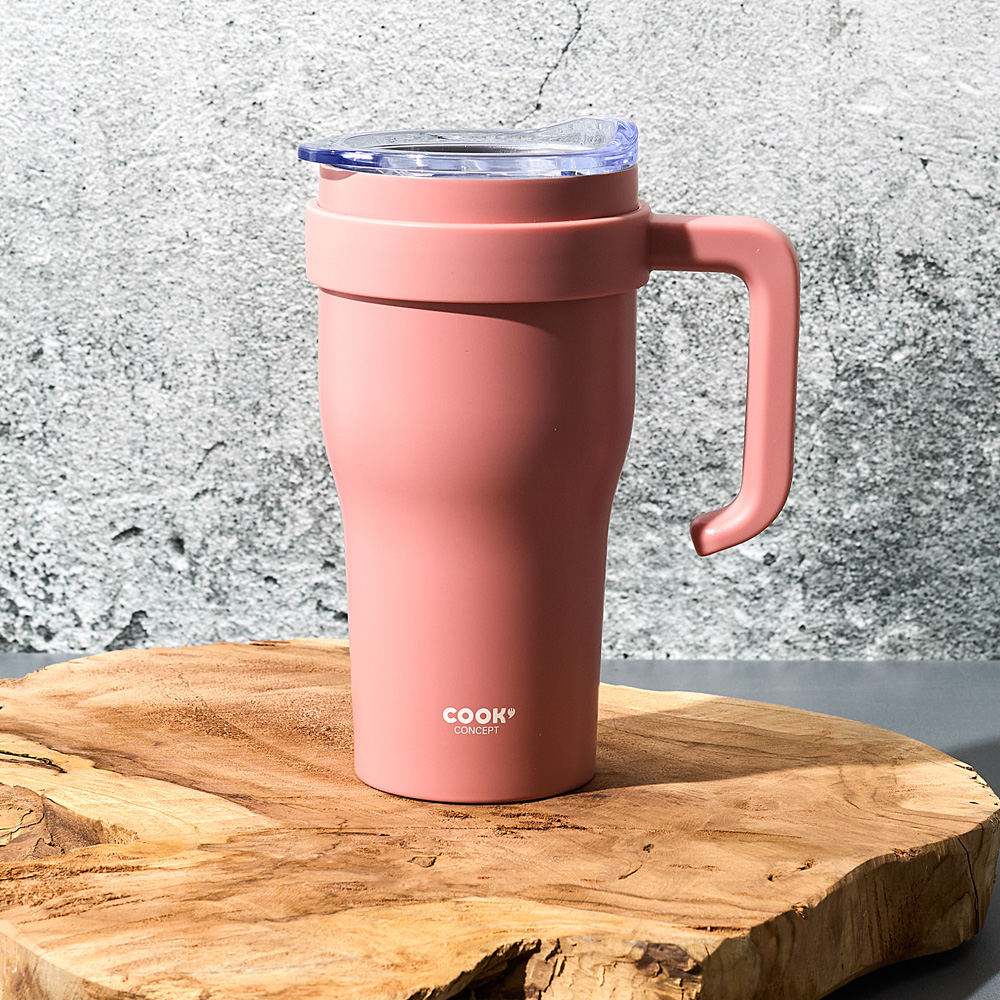 Una taza rosa con asa y tapa transparente descansa sobre madera.