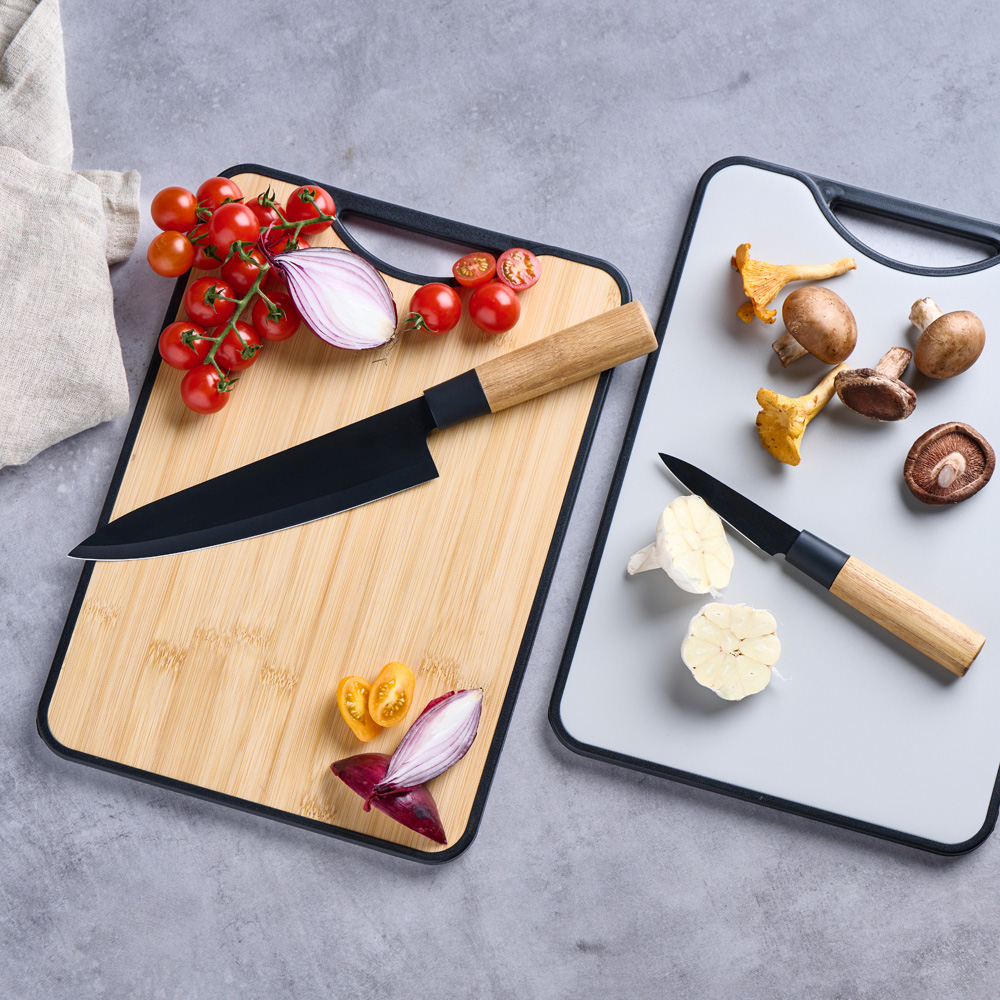 Un cuchillo con mango de madera y uno blanco sobre tablas de cortar con setas, tomates y cebollas.