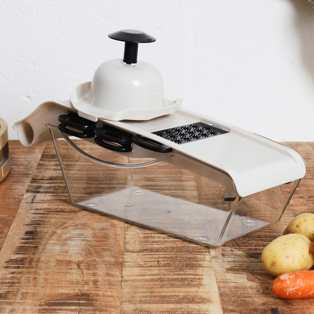 Un cortador de verduras blanco con recipiente transparente sobre mesa de madera.