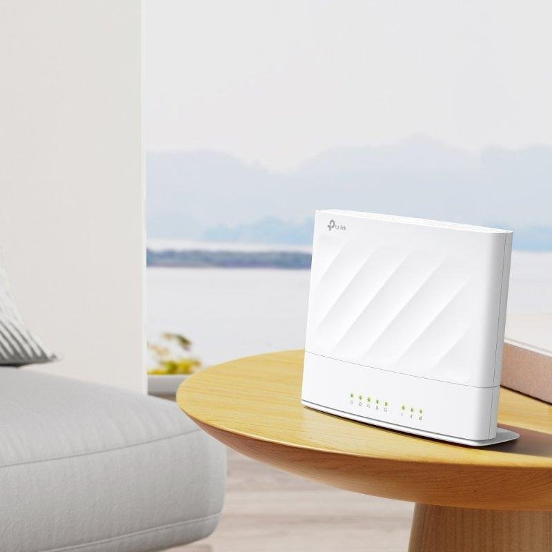 Un router TP-Link blanco sobre una mesa de madera junto a un sofá, con fondo marino borroso.