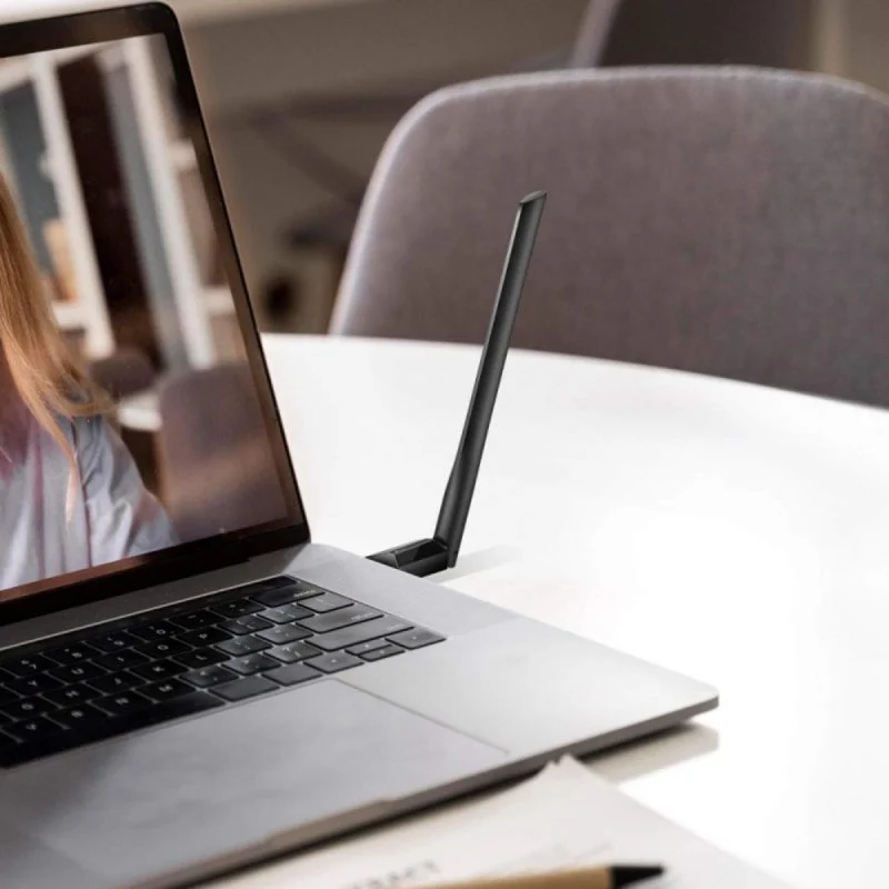 Un portátil con un adaptador WiFi en un escritorio con una silla de oficina detrás.