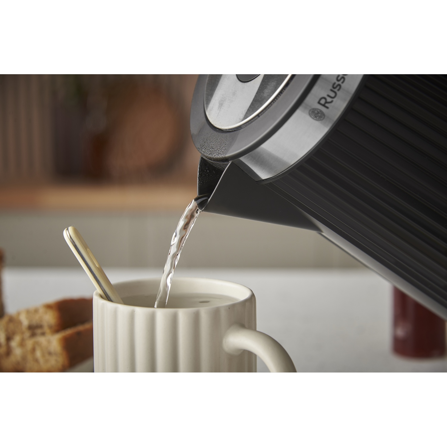Water stroomt uit een waterkoker in een mok met een lepel en brood.