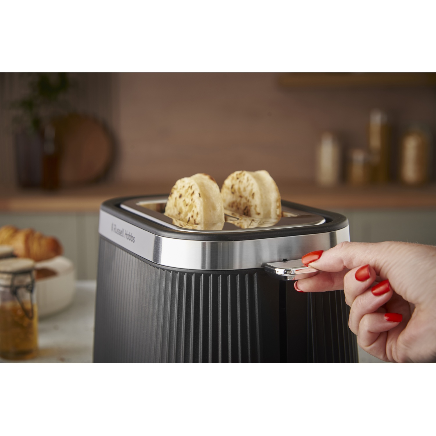 Une main aux ongles rouges actionne un grille-pain avec deux toasts.