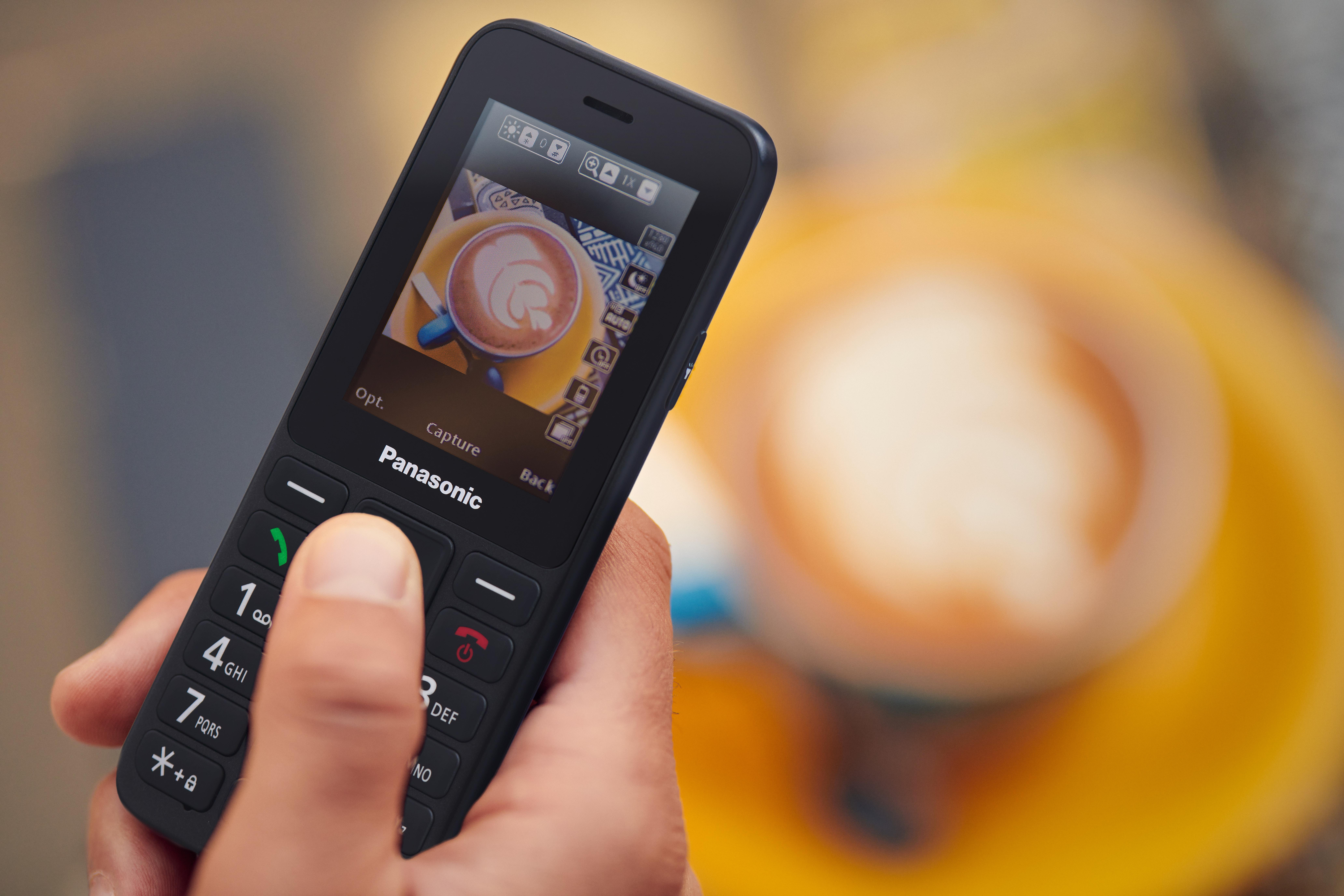 Eine Hand hält ein Panasonic-Telefon mit einer Kaffeetasse auf dem Bildschirm.