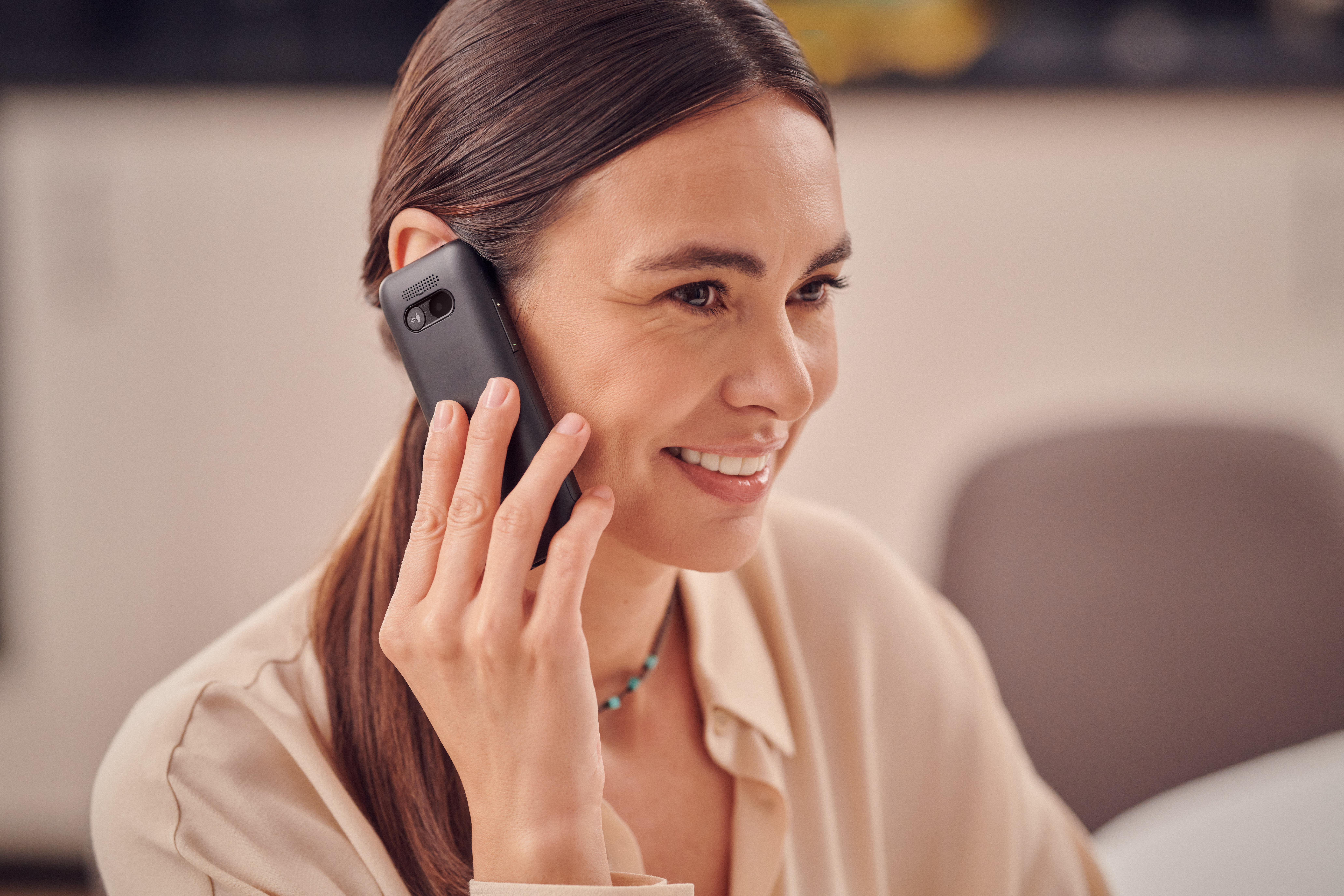 Eine Frau mit braunen Haaren telefoniert mit einem schwarzen Mobiltelefon.