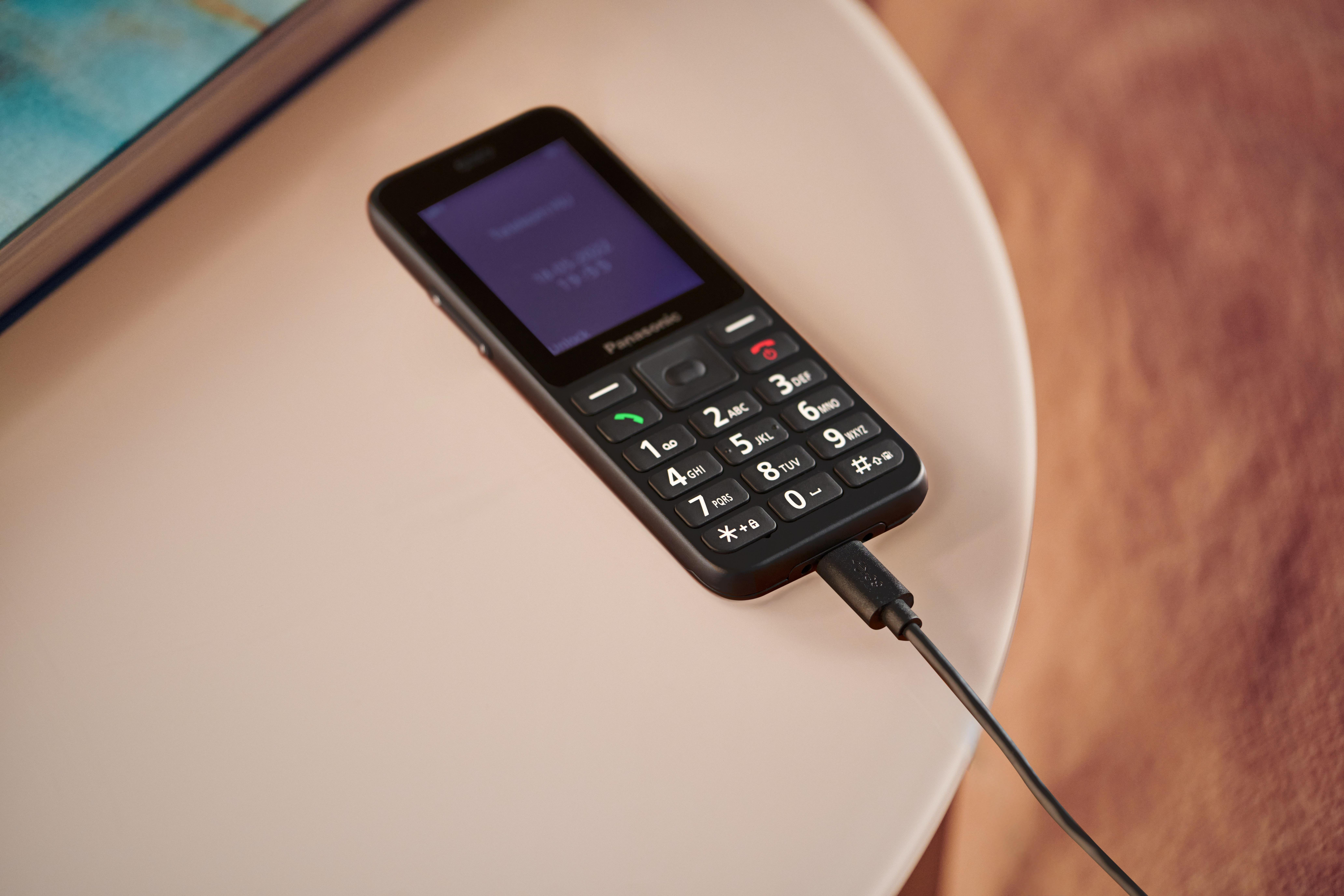 Ein schwarzes Panasonic-Handy wird über ein schwarzes Kabel aufgeladen.