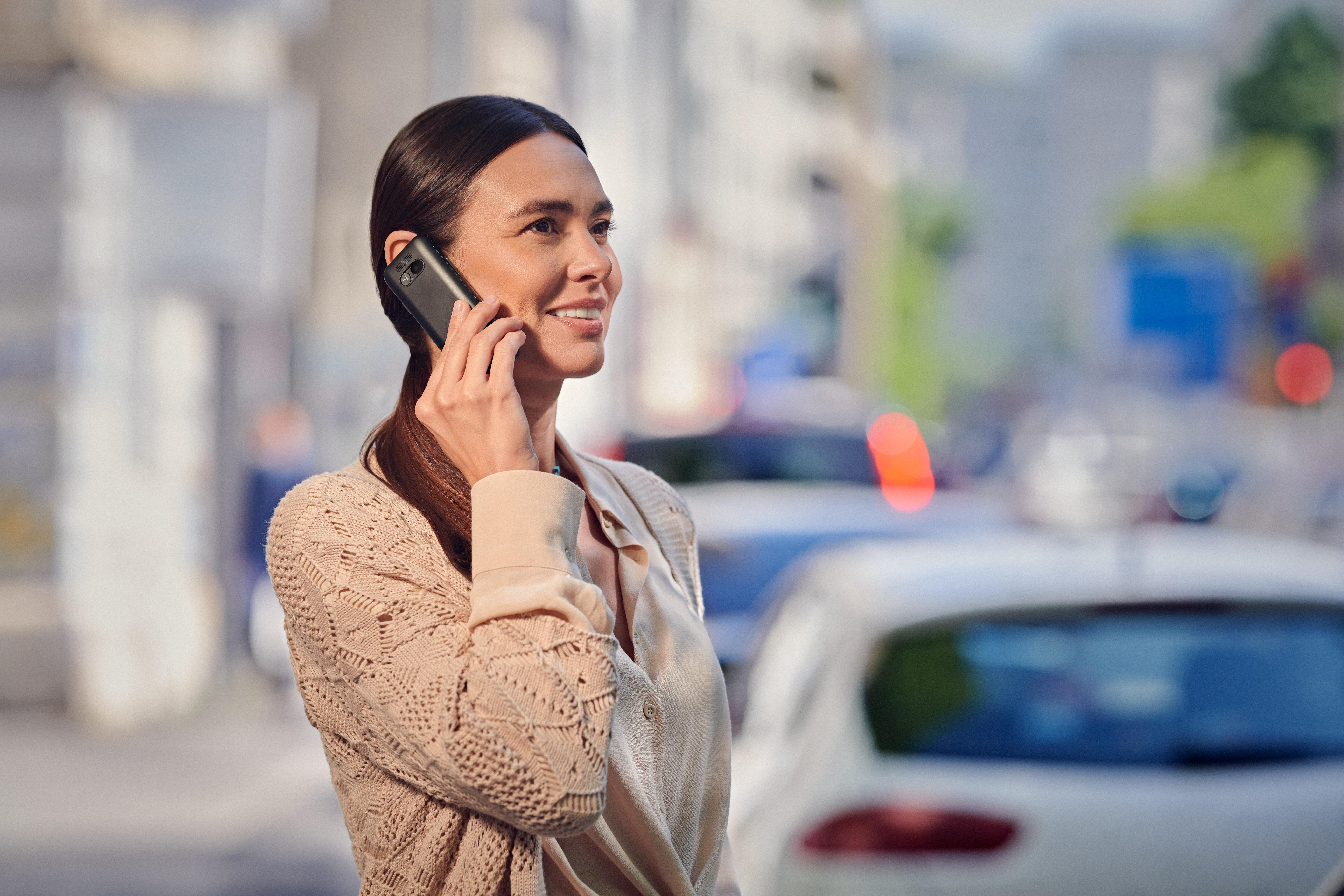 Eine Frau telefoniert auf der Straße mit Autos im Hintergrund.