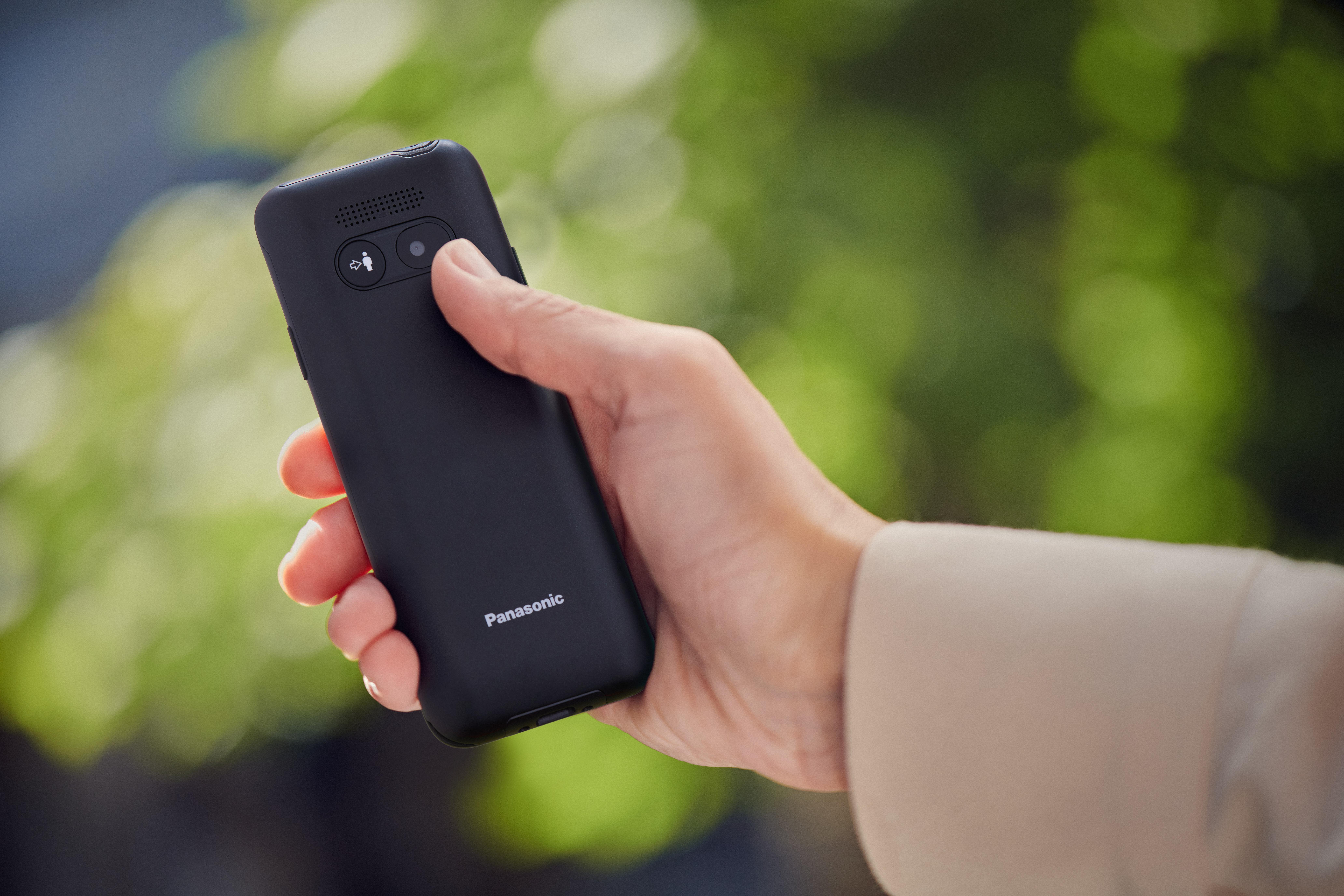 Eine Hand hält ein schwarzes Panasonic-Telefon mit einem Symbol und einem Knopf.