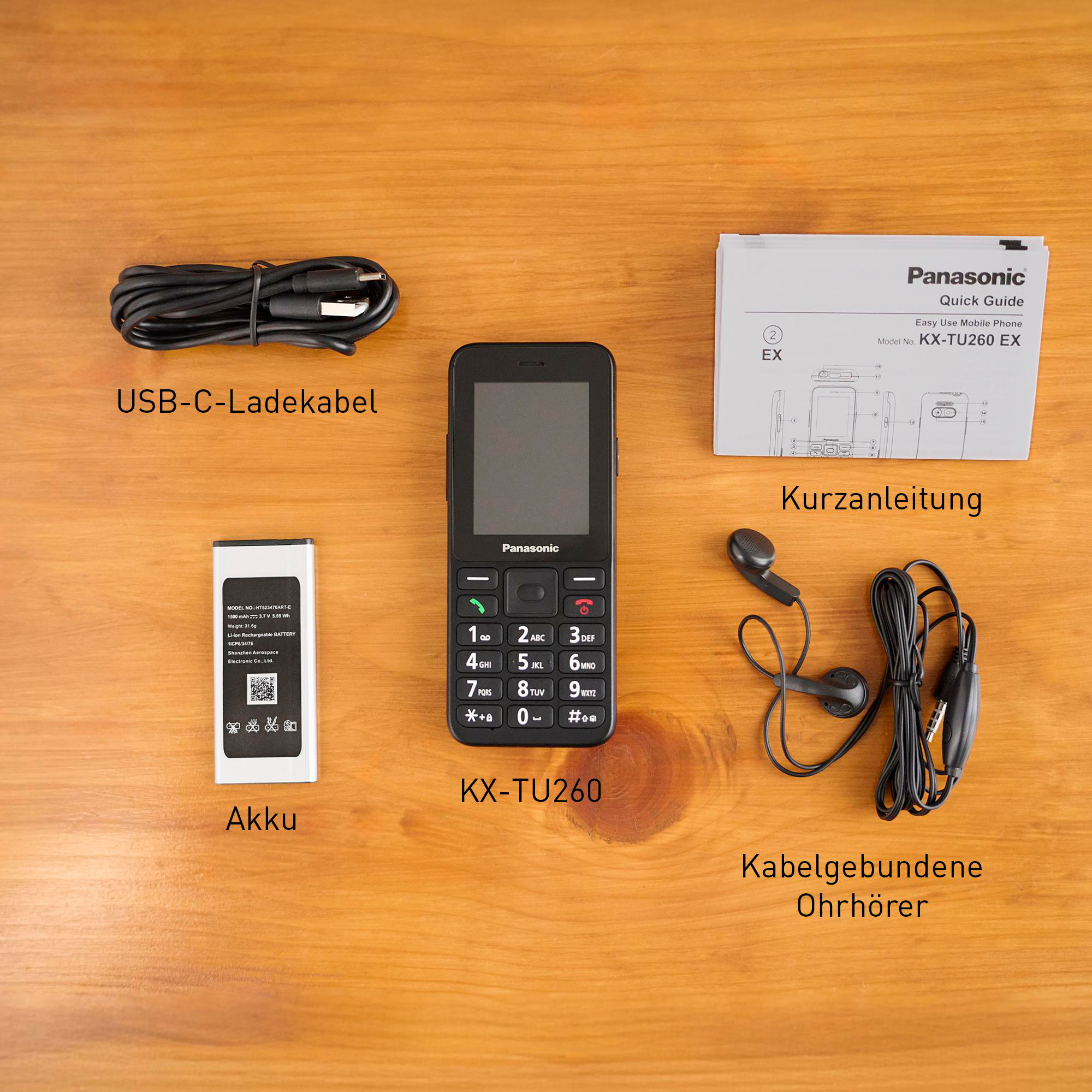 Ein Panasonic KX-TU260EX Handy mit Zubehör: Ladekabel, Akku, Ohrhörer und Anleitung.