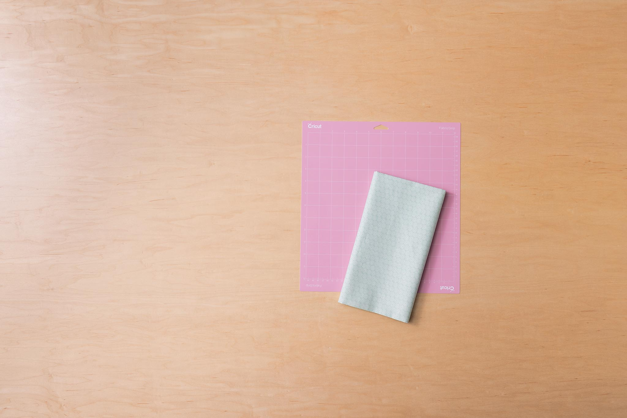 Una alfombrilla de corte rosa con tela yace sobre una mesa de madera.