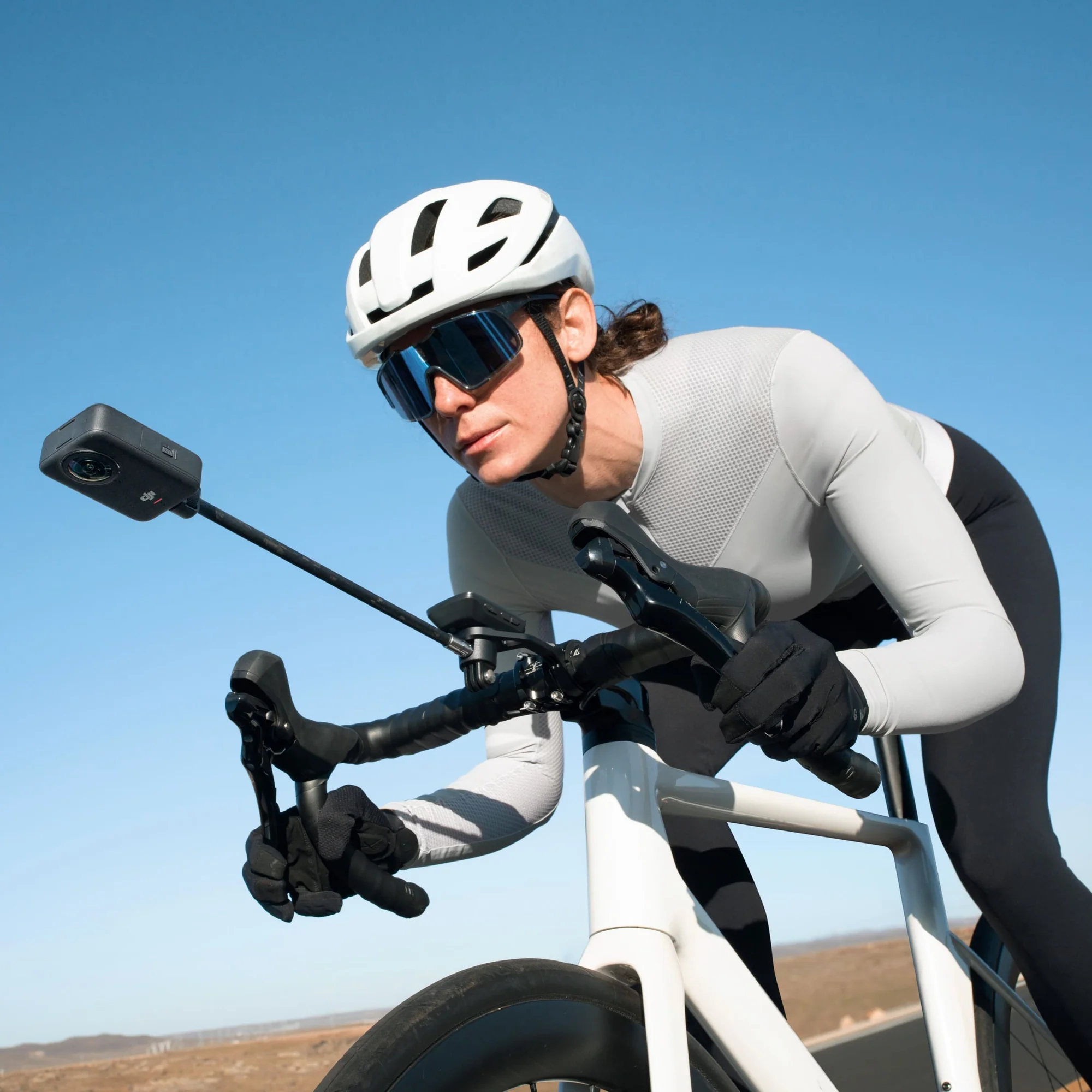 Kolarz w kasku i okularach na białym rowerze szosowym, kamera na kierownicy.