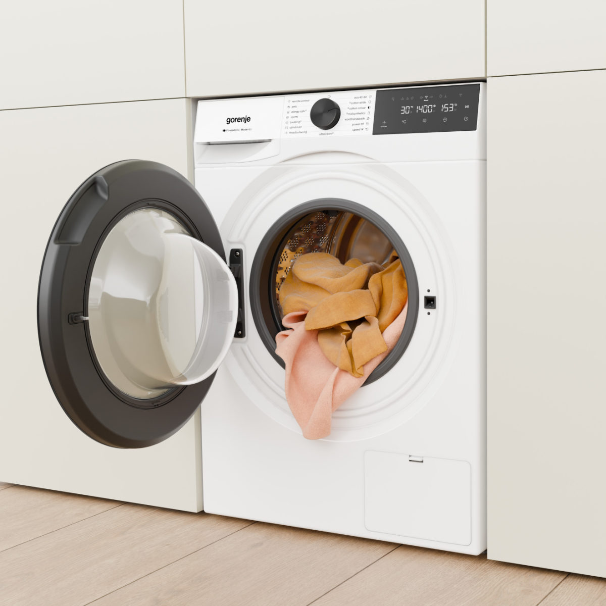 Fehér Gorenje mosógép nyitott ajtóval, benne ruhákkal.