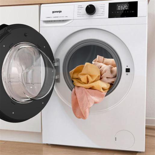 Fehér Gorenje mosógép nyitott ajtóval, pasztellszínű ruhákkal.
