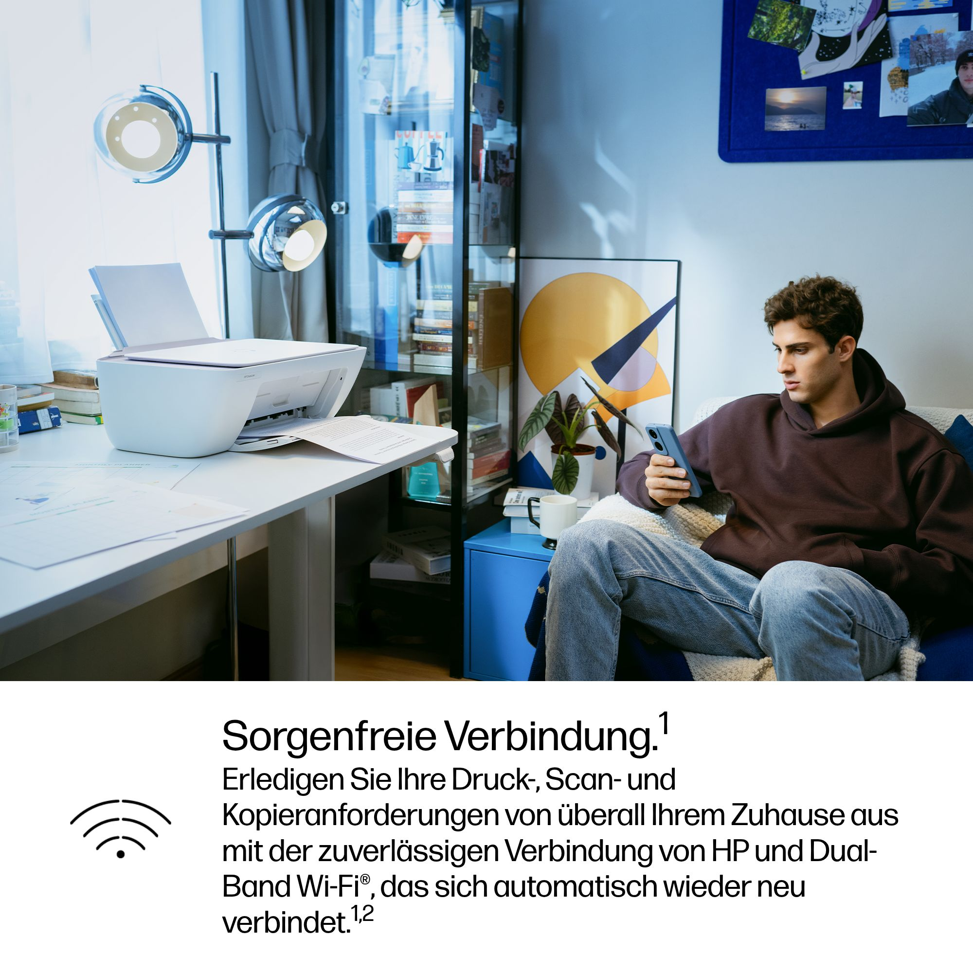 Ein Mann sitzt auf einem Sofa und blickt auf sein Handy, während ein Drucker im Hintergrund arbeitet.