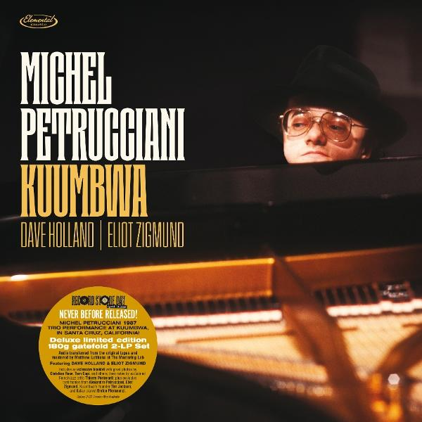 Michel Petrucciani auf einem Klavier, mit Hut und Brille, im Dunkeln.