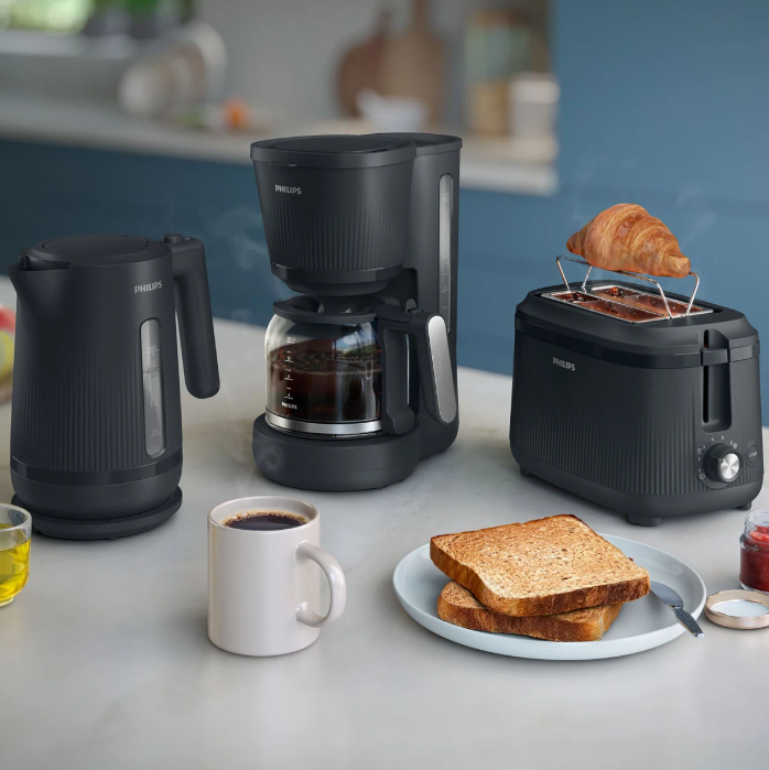 Czajnik, ekspres do kawy i toster czarne z artykułami śniadaniowymi na blacie.
