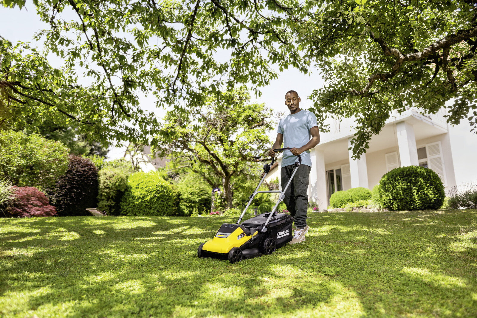 Mężczyzna pcha żółtą kosiarkę po zielonym trawniku przed domem.