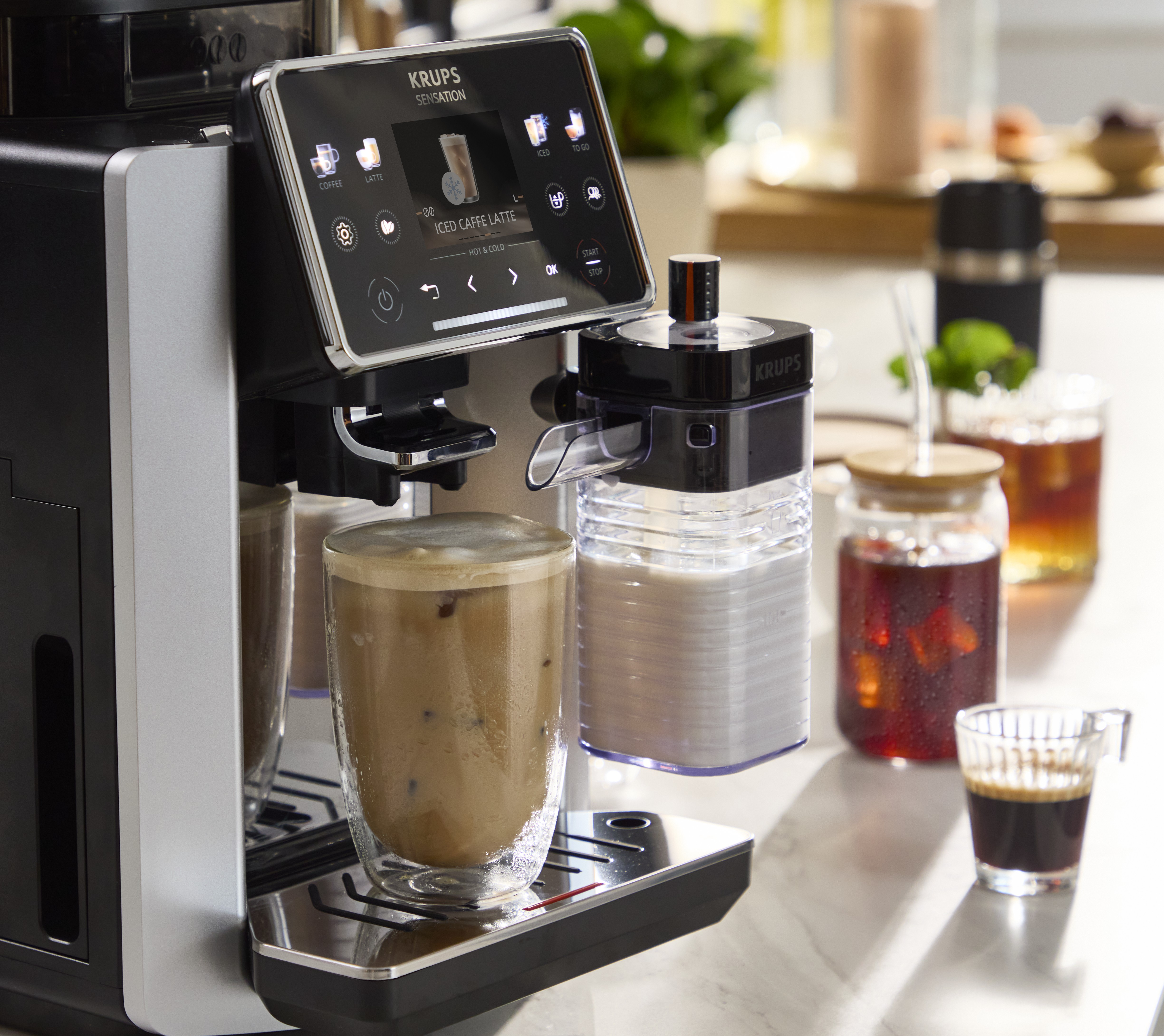 Eine Krups-Kaffeemaschine bereitet einen Eiskaffee Latte in einem doppelwandigen Glas zu.