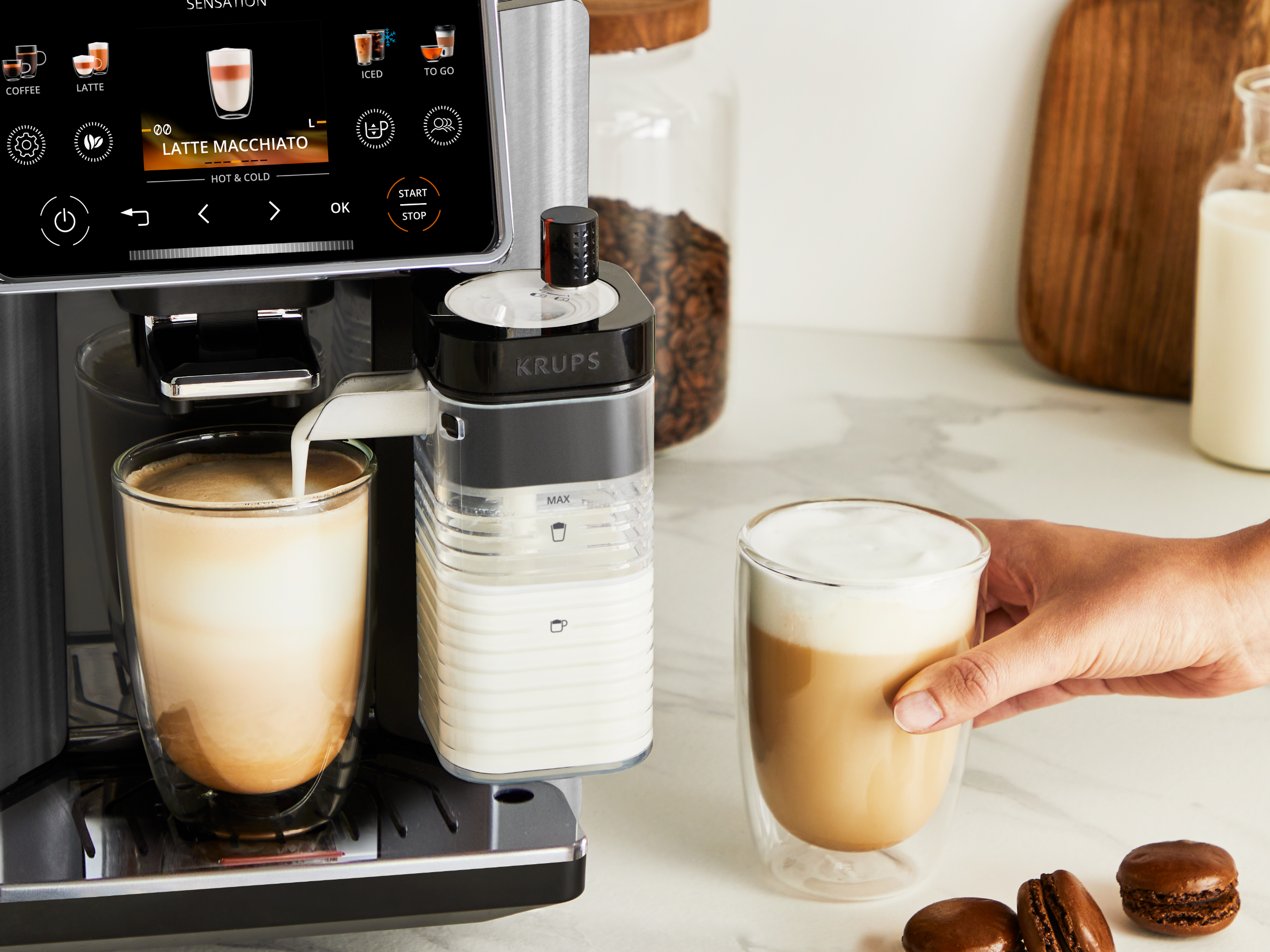 Kaffeemaschine brüht einen Latte Macchiato in ein Glas. Milchbehälter daneben.