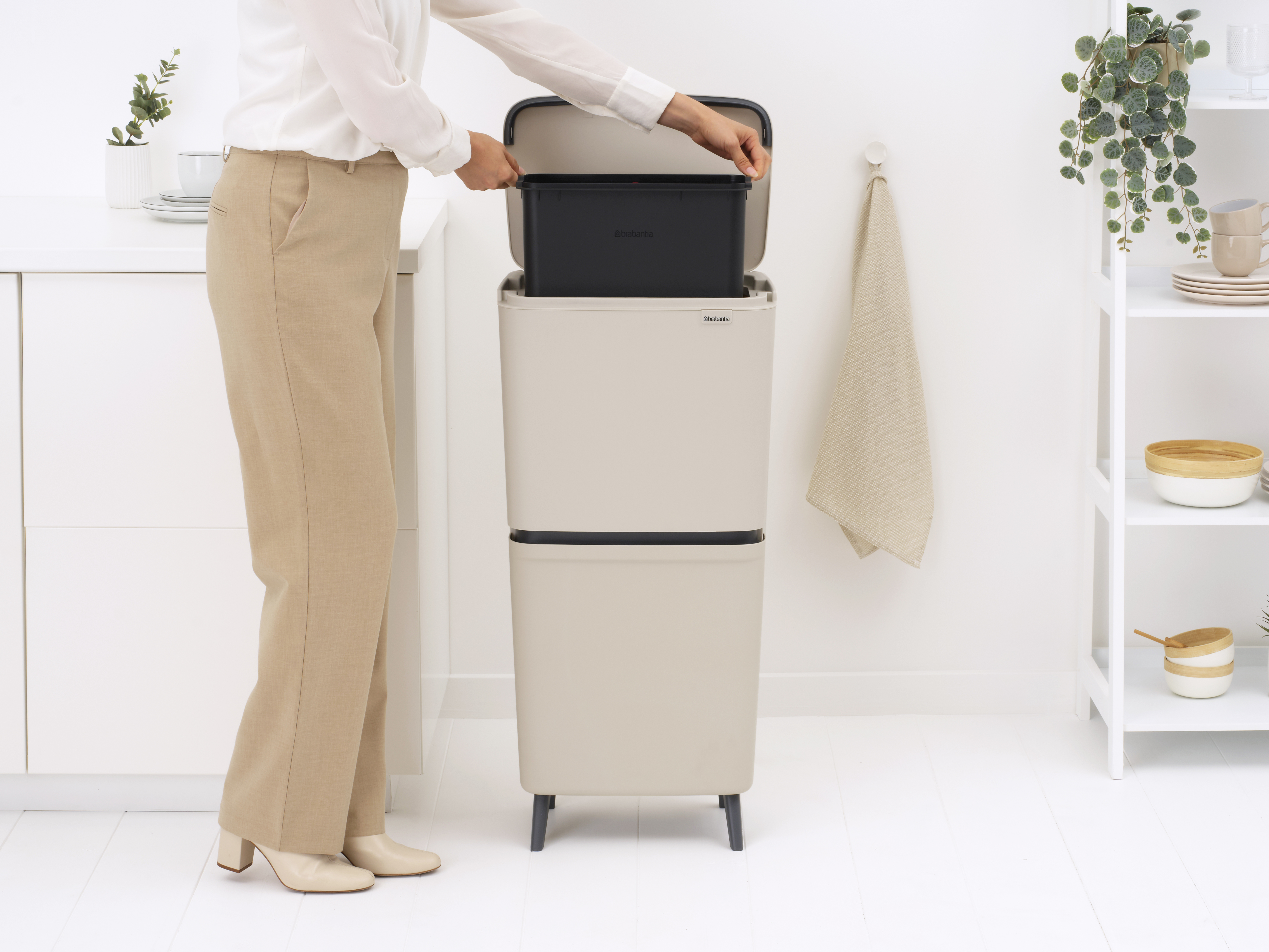 Eine Person in beiger Hose und weißem Hemd stellt eine schwarze Tonne in eine beige Tonne.