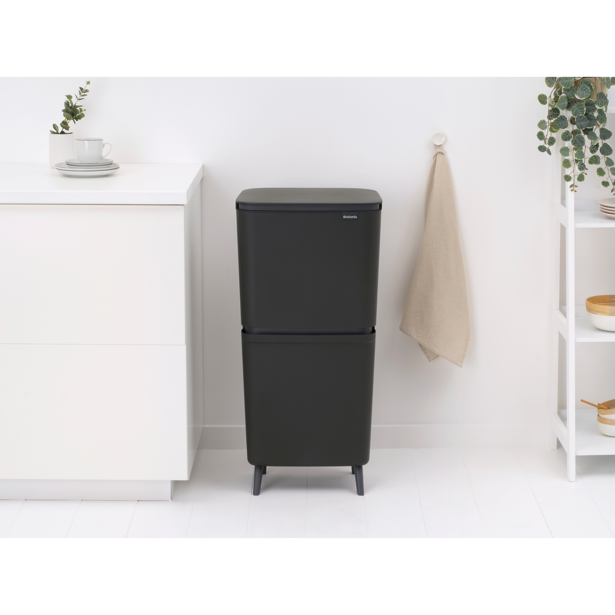 Ein schwarzer Mülltrenner steht auf weißem Boden neben einem weißen Schrank.