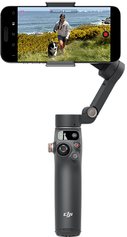 Gimbal nero con smartphone che riprende donna e cane su costa erbosa.