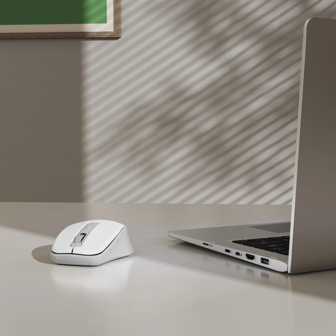 Biała mysz obok otwartego laptopa na biurku.