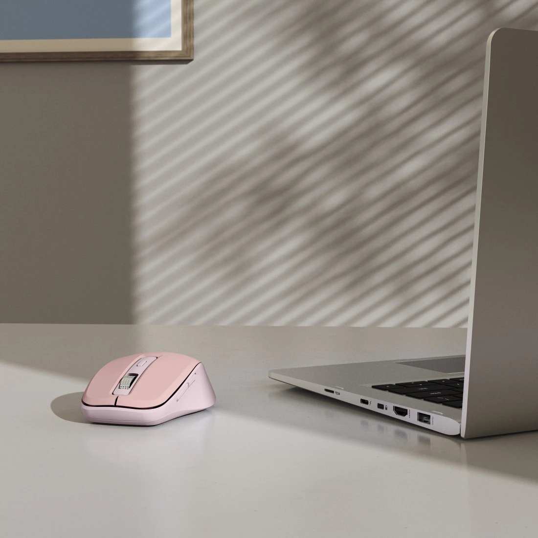 Różowa mysz bezprzewodowa leży na biurku obok otwartego laptopa.