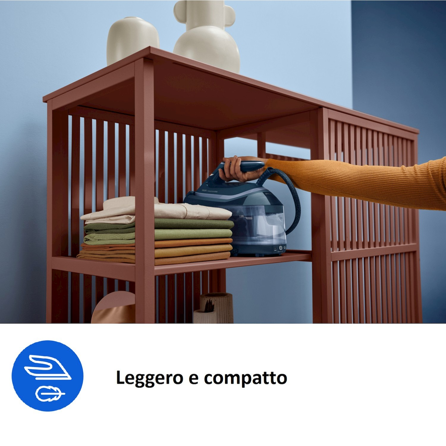 Mano tiene vaporiera per abiti su scaffale con vestiti. Due vasi in cima.