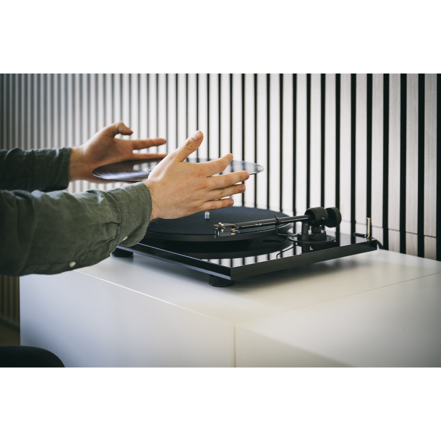 Persona che posiziona un disco su un giradischi con sfondo a strisce bianche e nere.