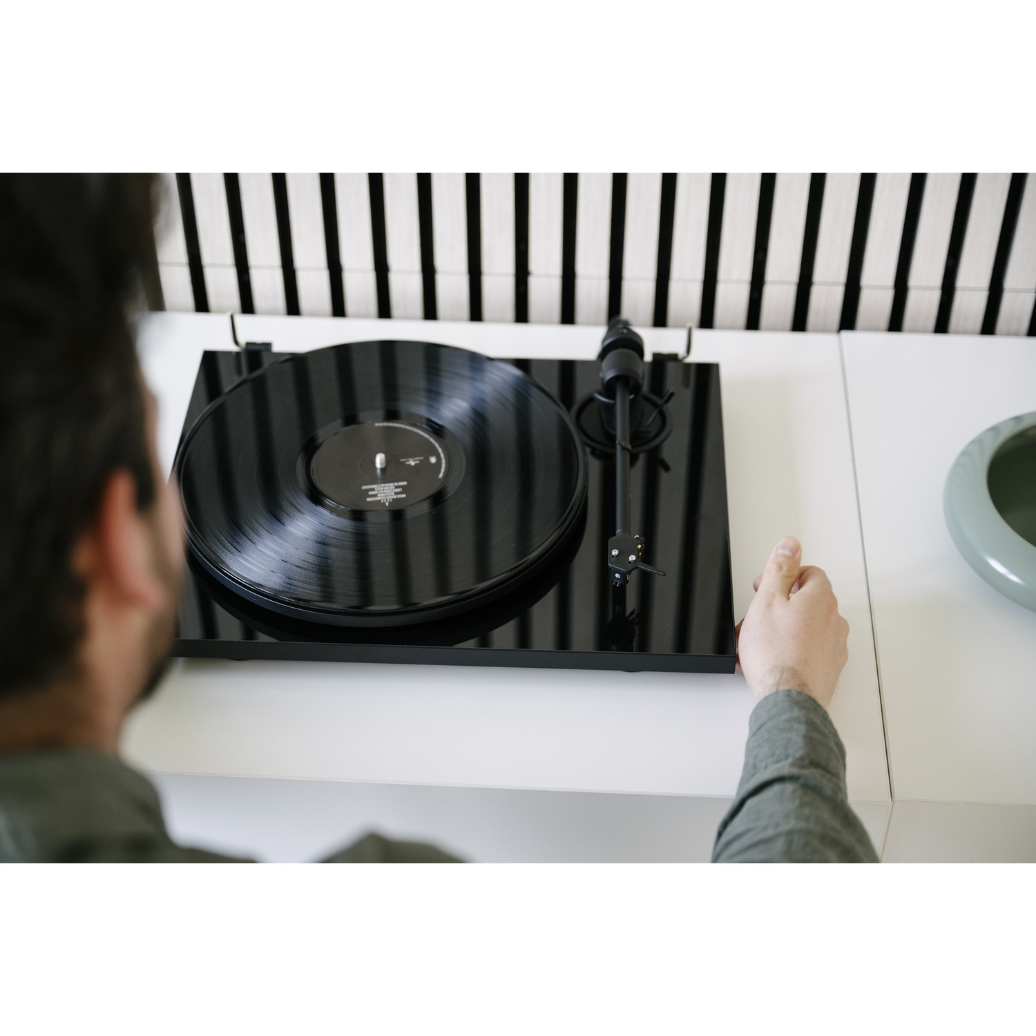 Un uomo aziona un giradischi con un disco in vinile nero su un tavolo bianco.