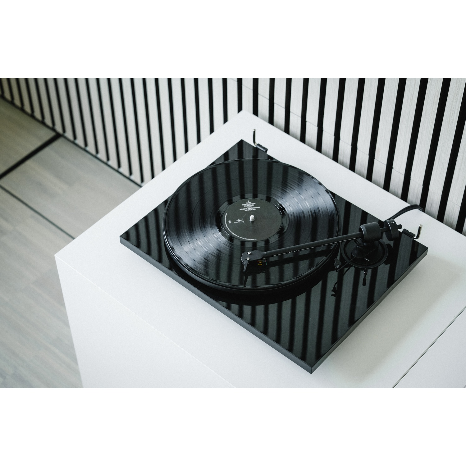 Giradischi nero con vinile su tavolo bianco davanti a parete a righe.