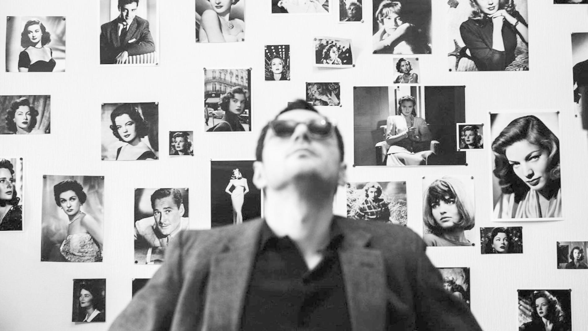 Mann im Vordergrund blickt auf Wand voller Schwarz-Weiß-Fotos von Schauspielerinnen.