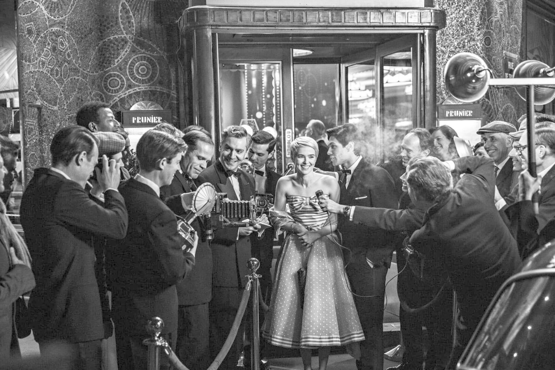 Eine Frau in einem gepunkteten Kleid posiert für Fotografen mit Blitzlichtgeräten.