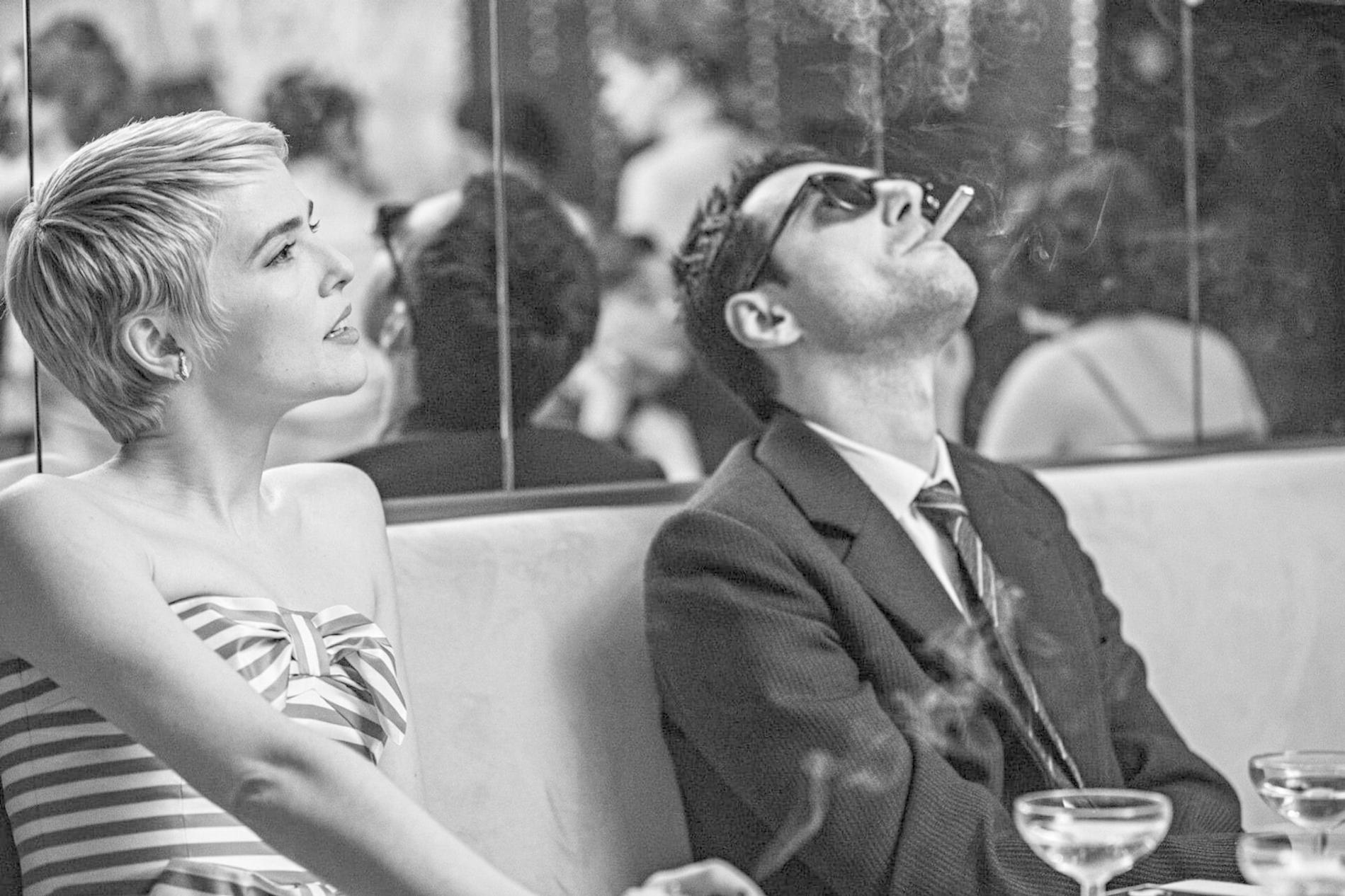 Eine Frau mit kurzem Haar und ein Mann mit Sonnenbrille rauchen in einem Restaurant.