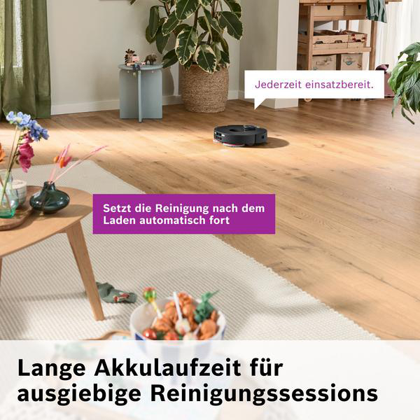 Ein Saugroboter fährt auf einem Holzboden, mit Blumen auf einem Tisch im Vordergrund.