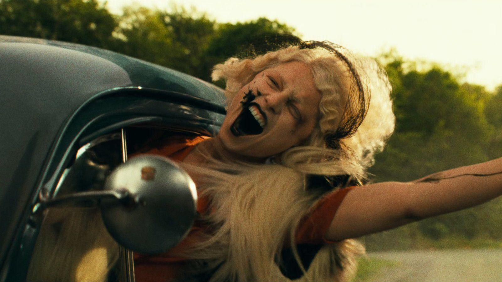 Eine Frau mit blondem Haar und schwarzem Make-up schreit aus einem Auto.