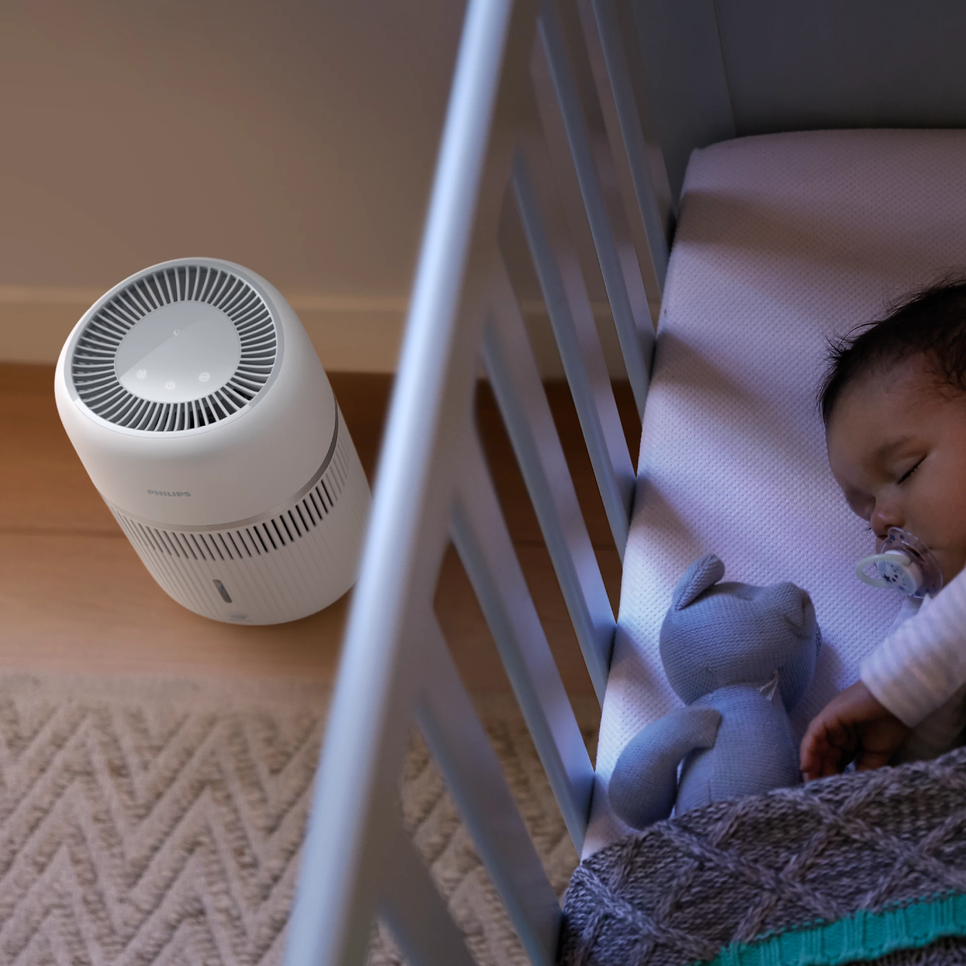 Un purificateur d'air blanc à côté d'un lit de bébé où dort un bébé.