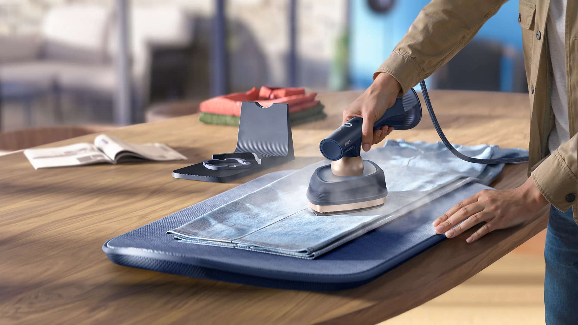 Una mano tiene un vaporizzatore per abiti, che vapore una camicia blu su un asse da stiro.
