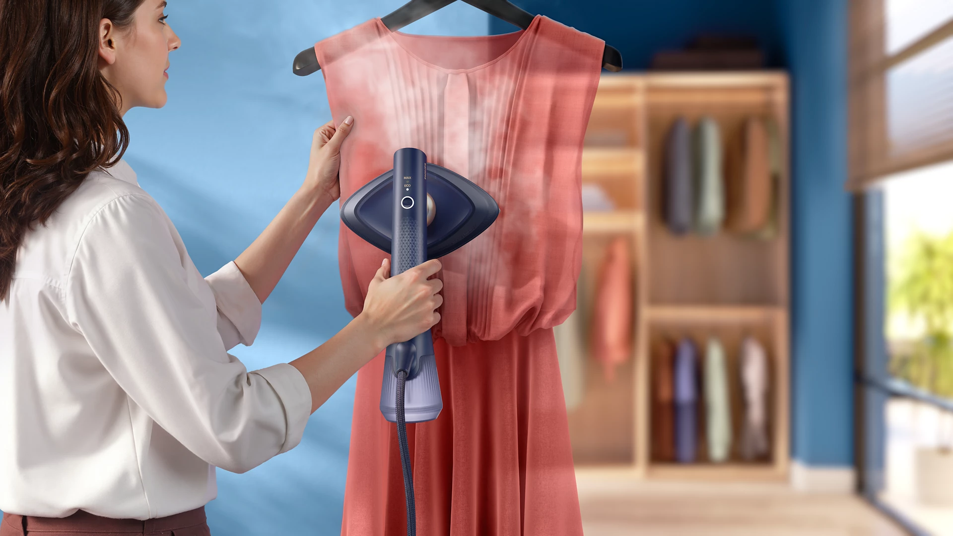 Una donna stira un vestito rosa con un vaporizzatore portatile in un armadio.