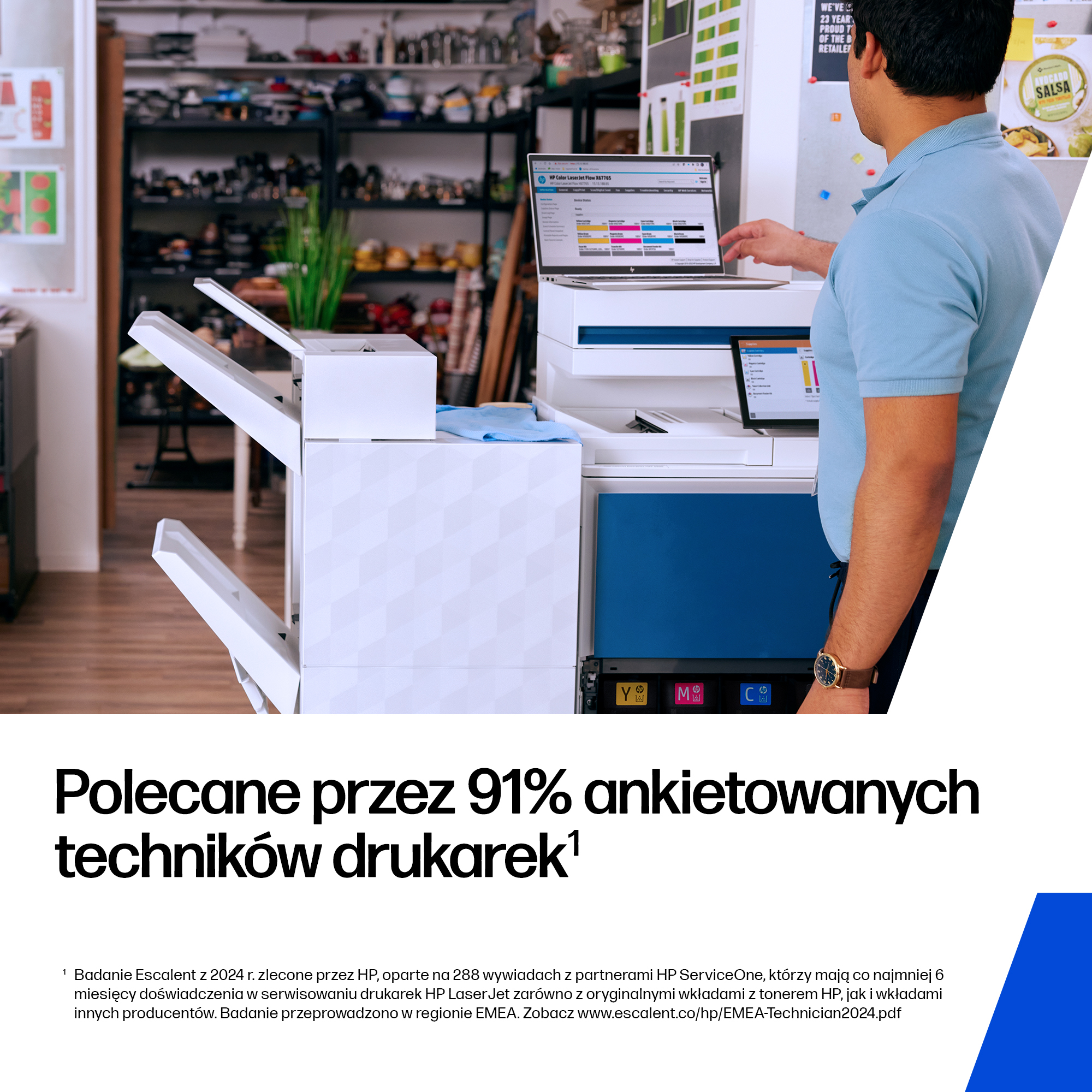 Mężczyzna w niebieskiej koszulce polo stoi przy drukarce, patrząc na ekran laptopa.