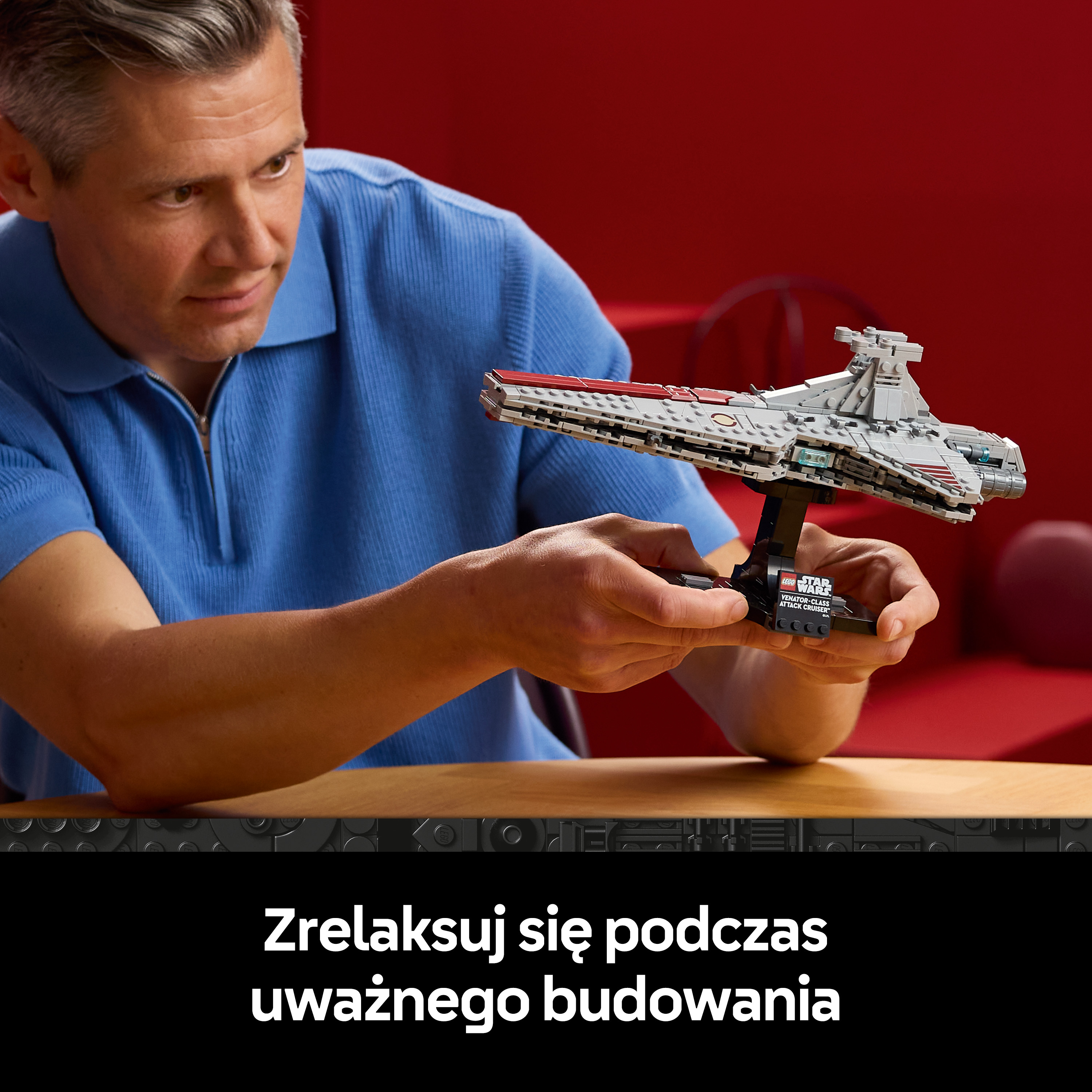 Mężczyzna w niebieskiej koszuli trzyma szary statek kosmiczny Lego.