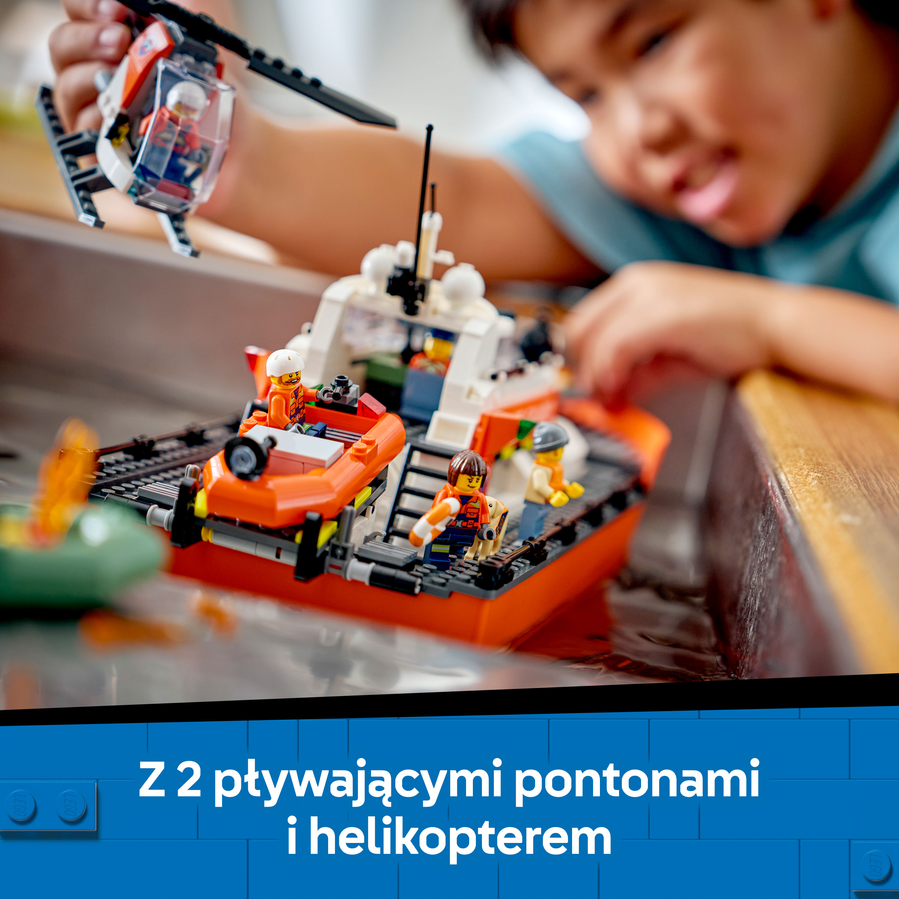 Chłopiec bawi się łodziami Lego i helikopterem w wodzie.