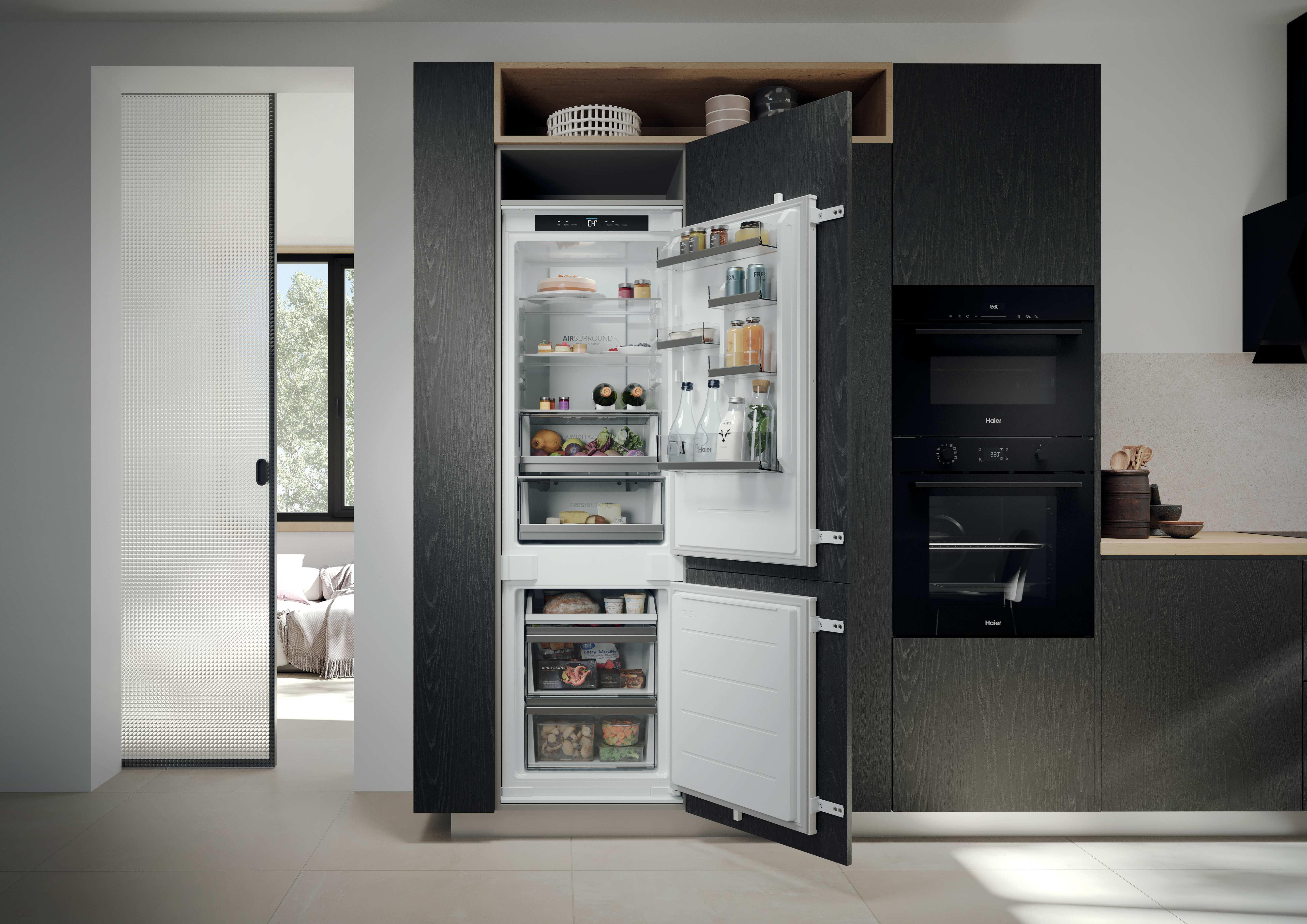 Offener Kühlschrank mit Lebensmitteln und zwei Öfen daneben in einer modernen Küche.