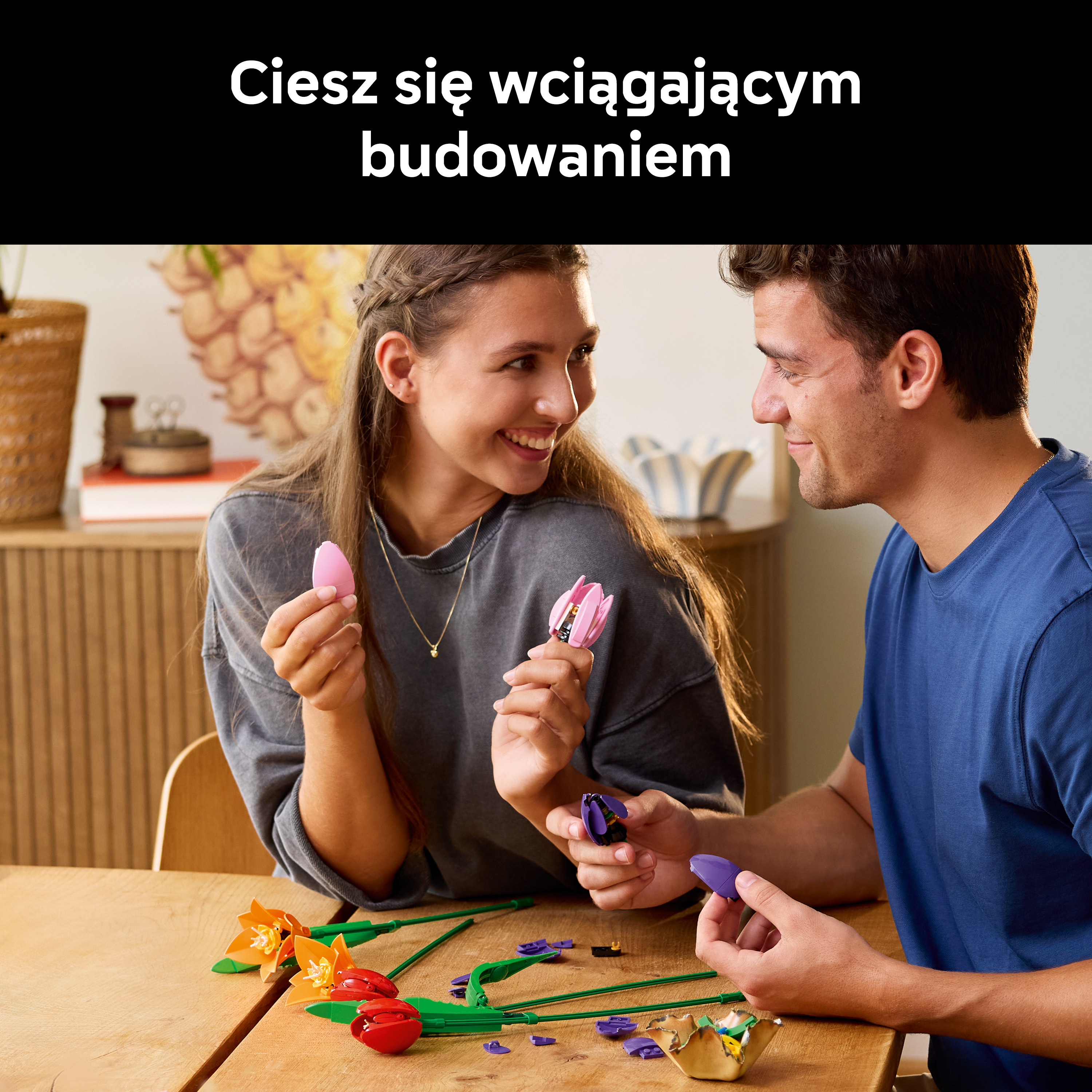 Mężczyzna i kobieta budują kolorowe tulipany z klocków Lego przy drewnianym stole.