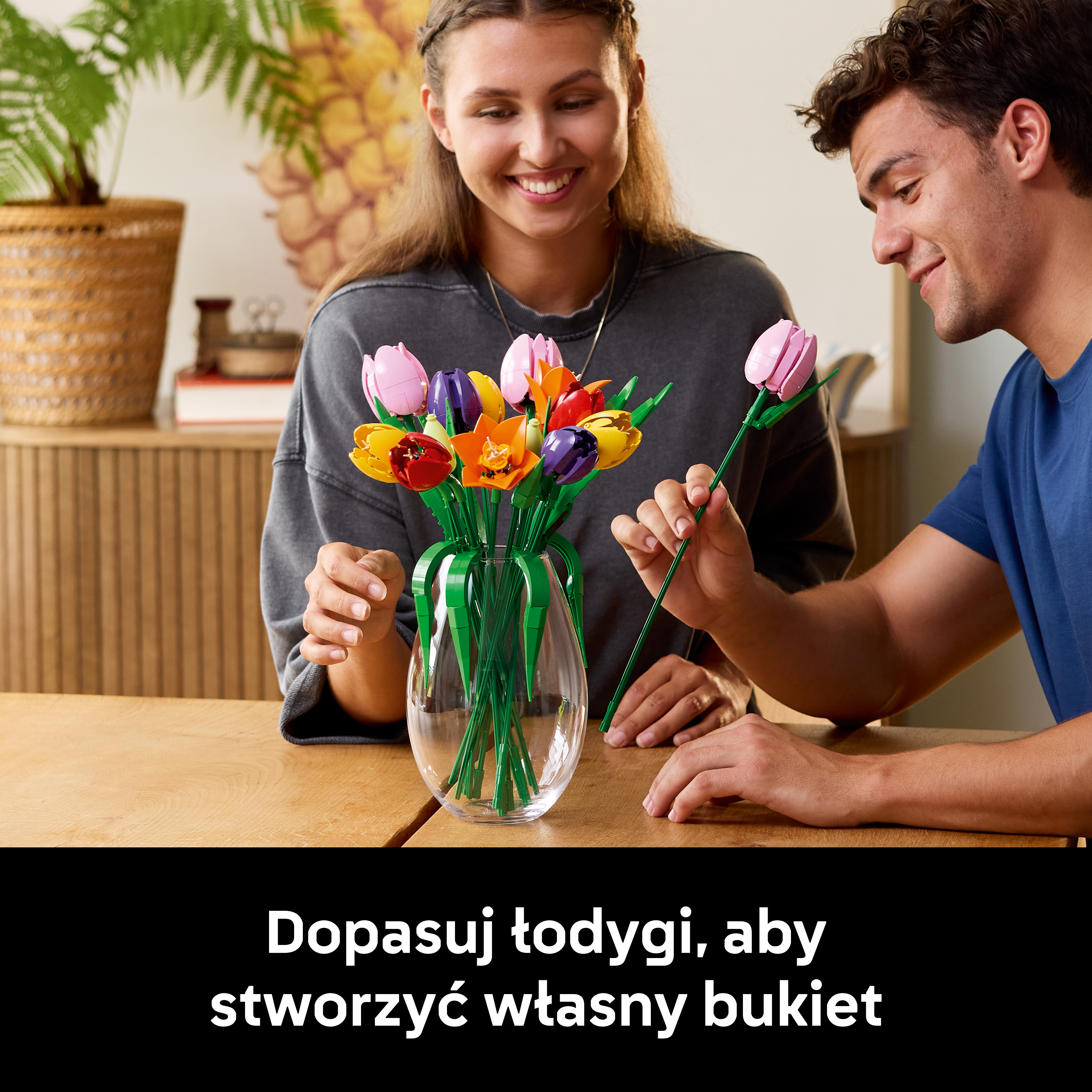 Mężczyzna i kobieta uśmiechają się nad bukietem kolorowych tulipanów Lego w szklanym wazonie.