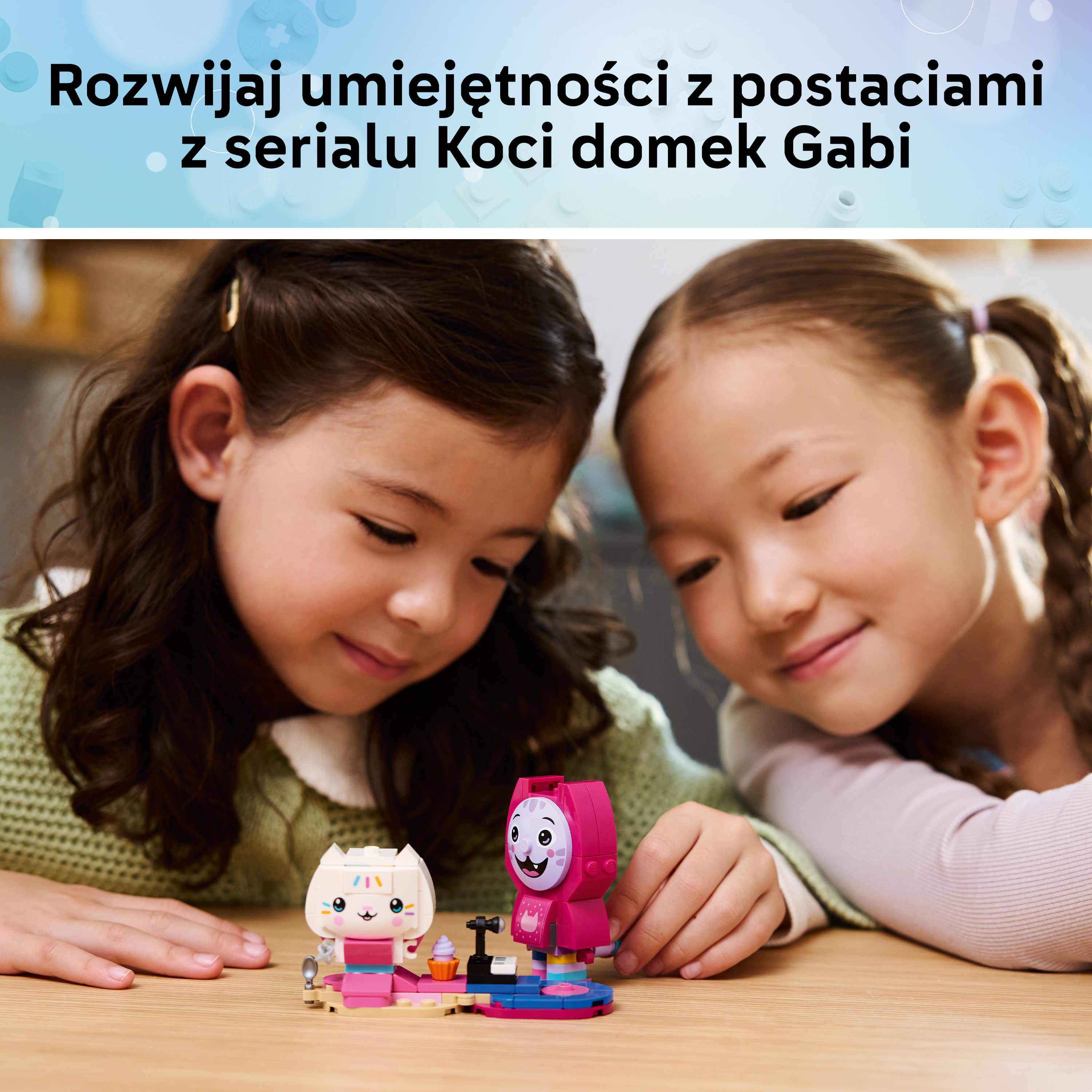 Dwie dziewczynki patrzą na figurki Lego na drewnianym stole. Biały kotek i różowa postać.